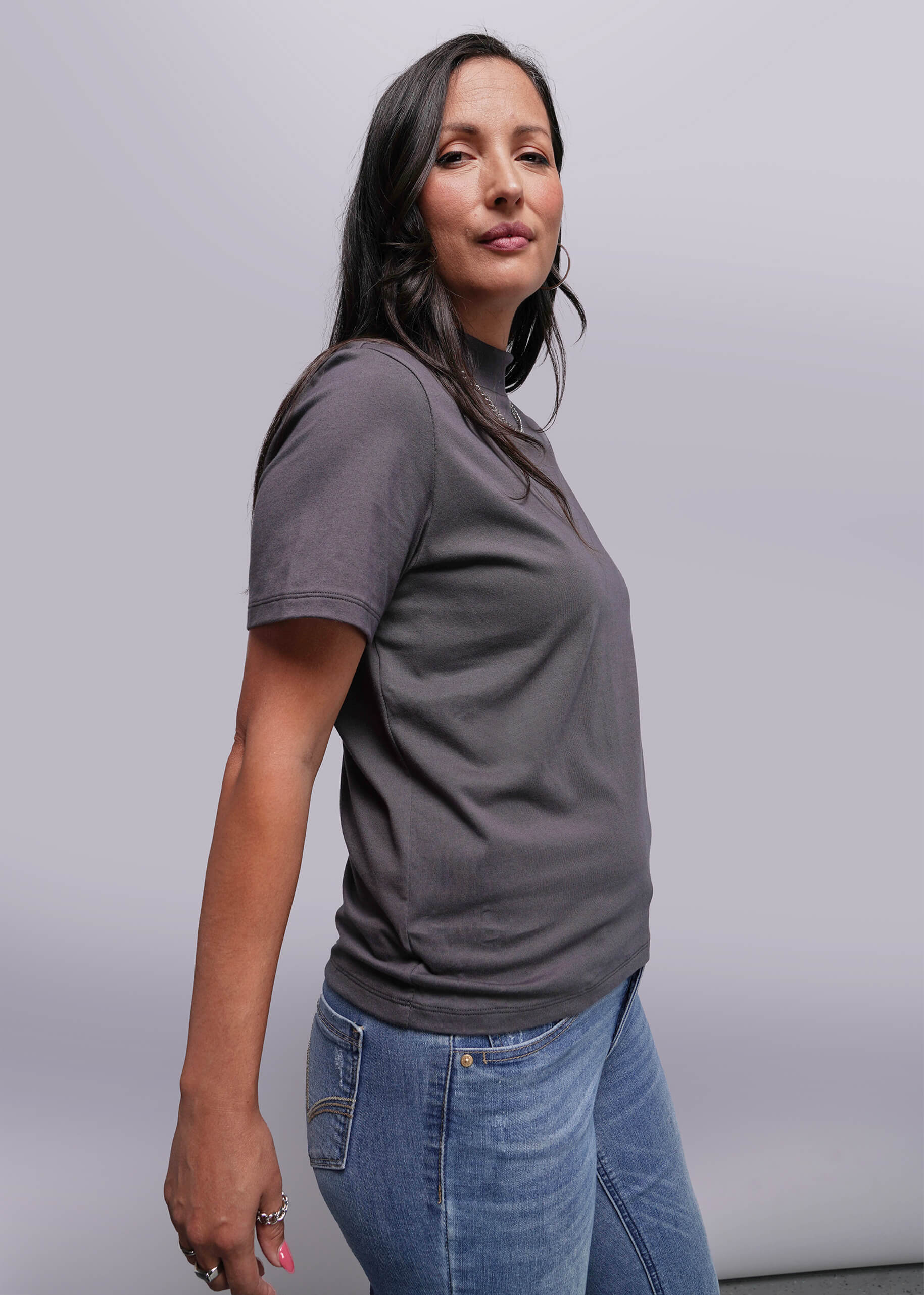 S=Woman wearing a gray t-shirt and blue jeans against a plain background