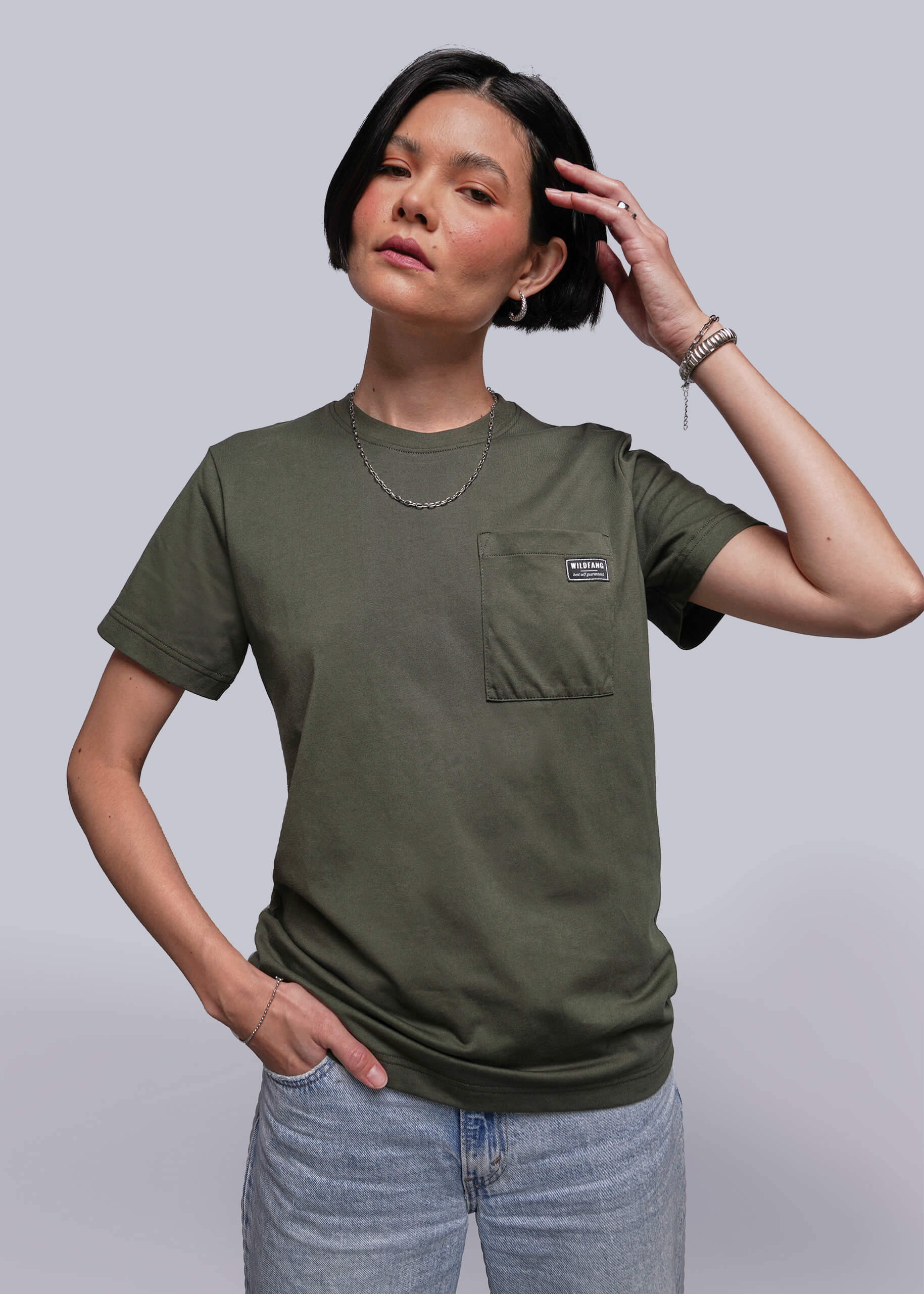 Person wearing an olive green t-shirt with a pocket on a plain background