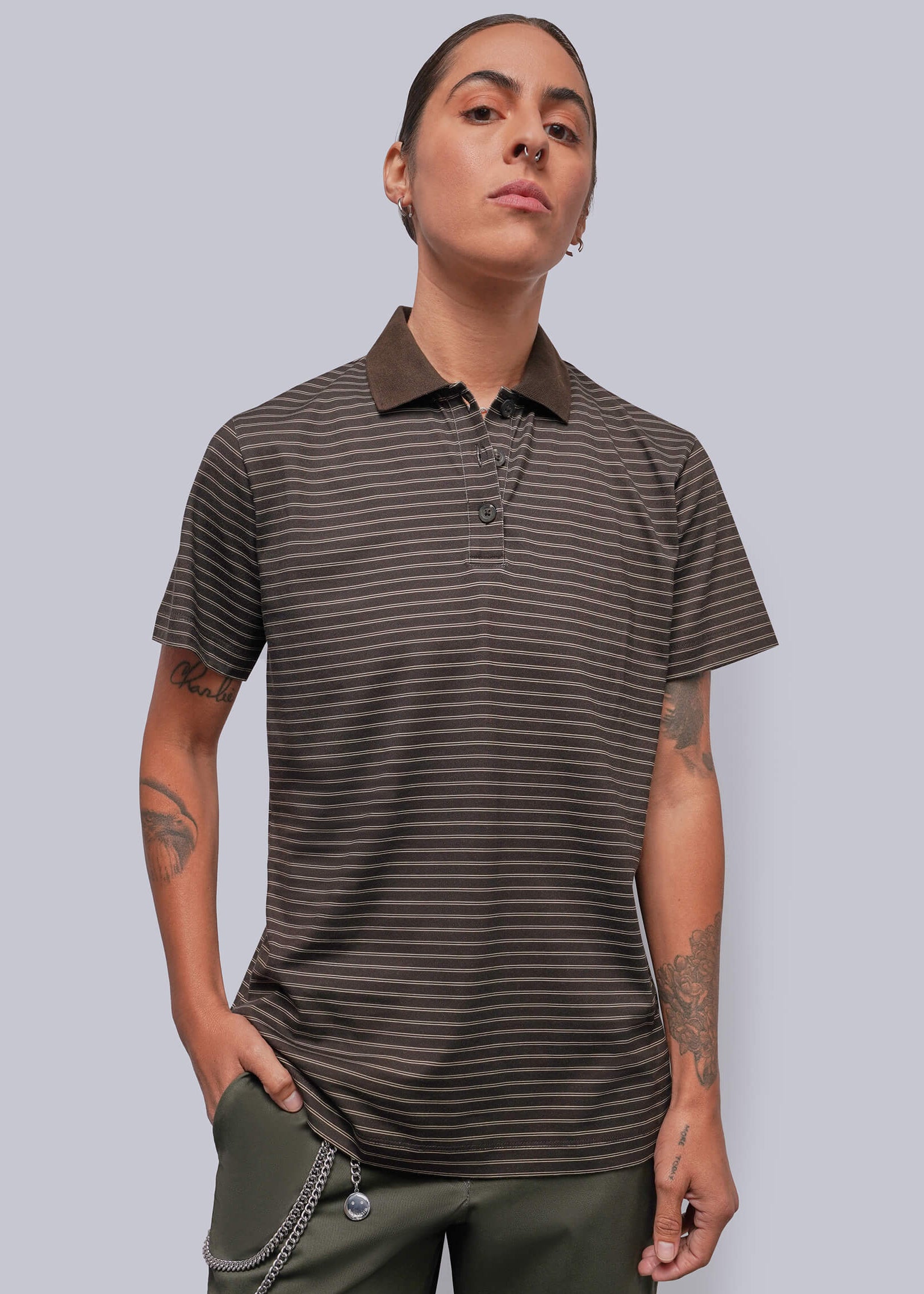 A model wearing a dark brown and black horizontally striped short-sleeve polo shirt with a solid dark brown collar, paired with olive green pants, against a solid gray background.