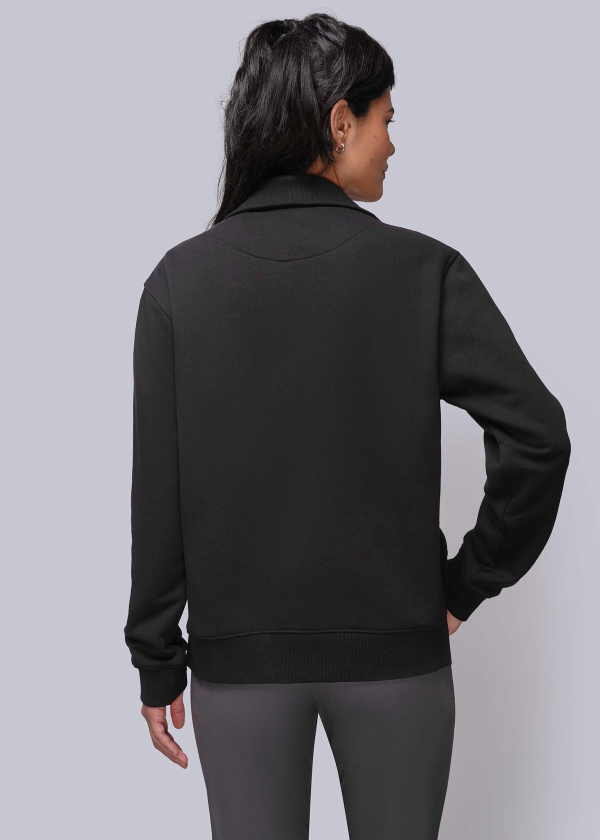 S=A woman shown from the back wearing a black long-sleeve zip-up jacket and dark gray pants against a light gray studio background.