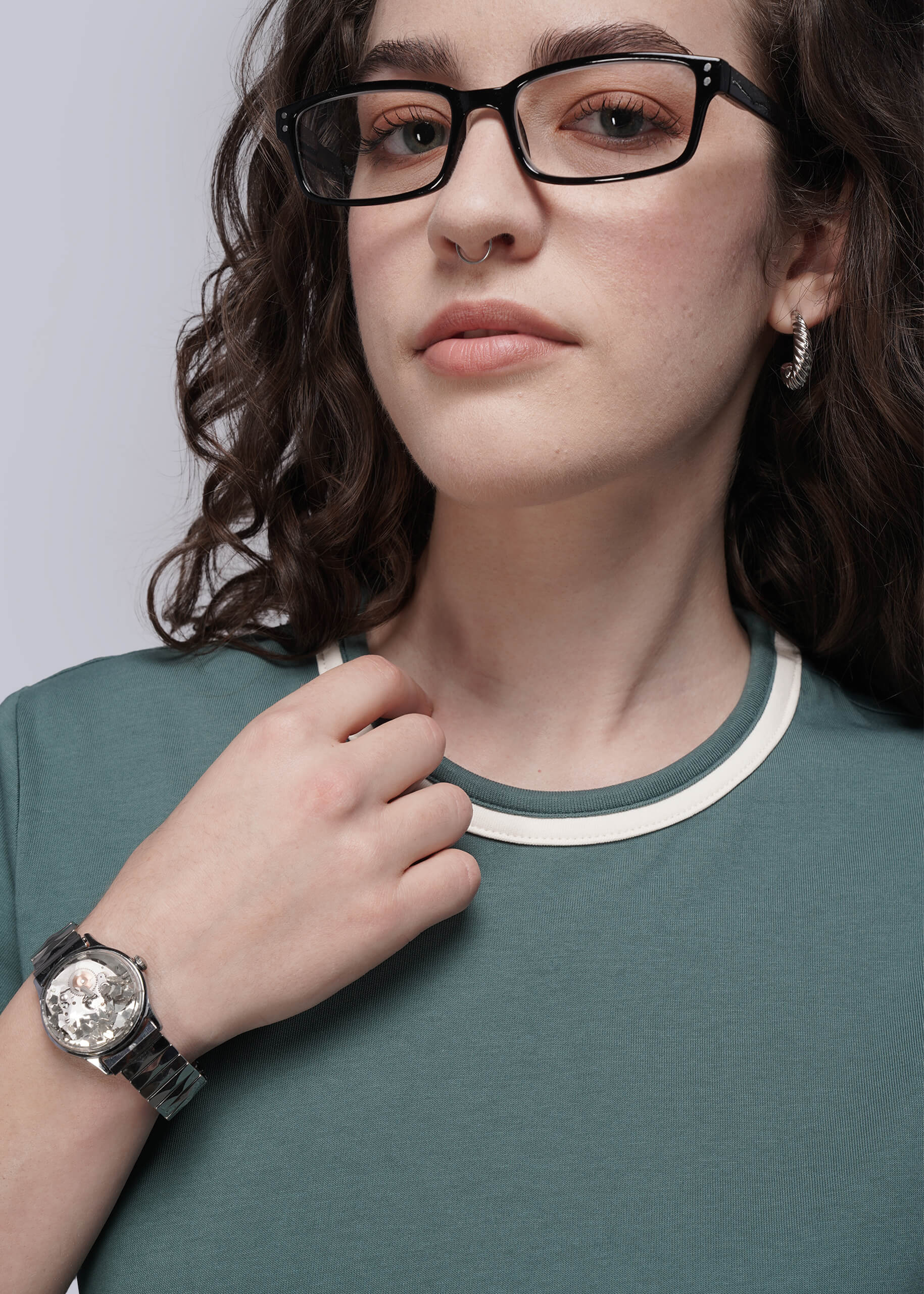 Person wearing glasses, a watch, and a teal tee with a neutral background