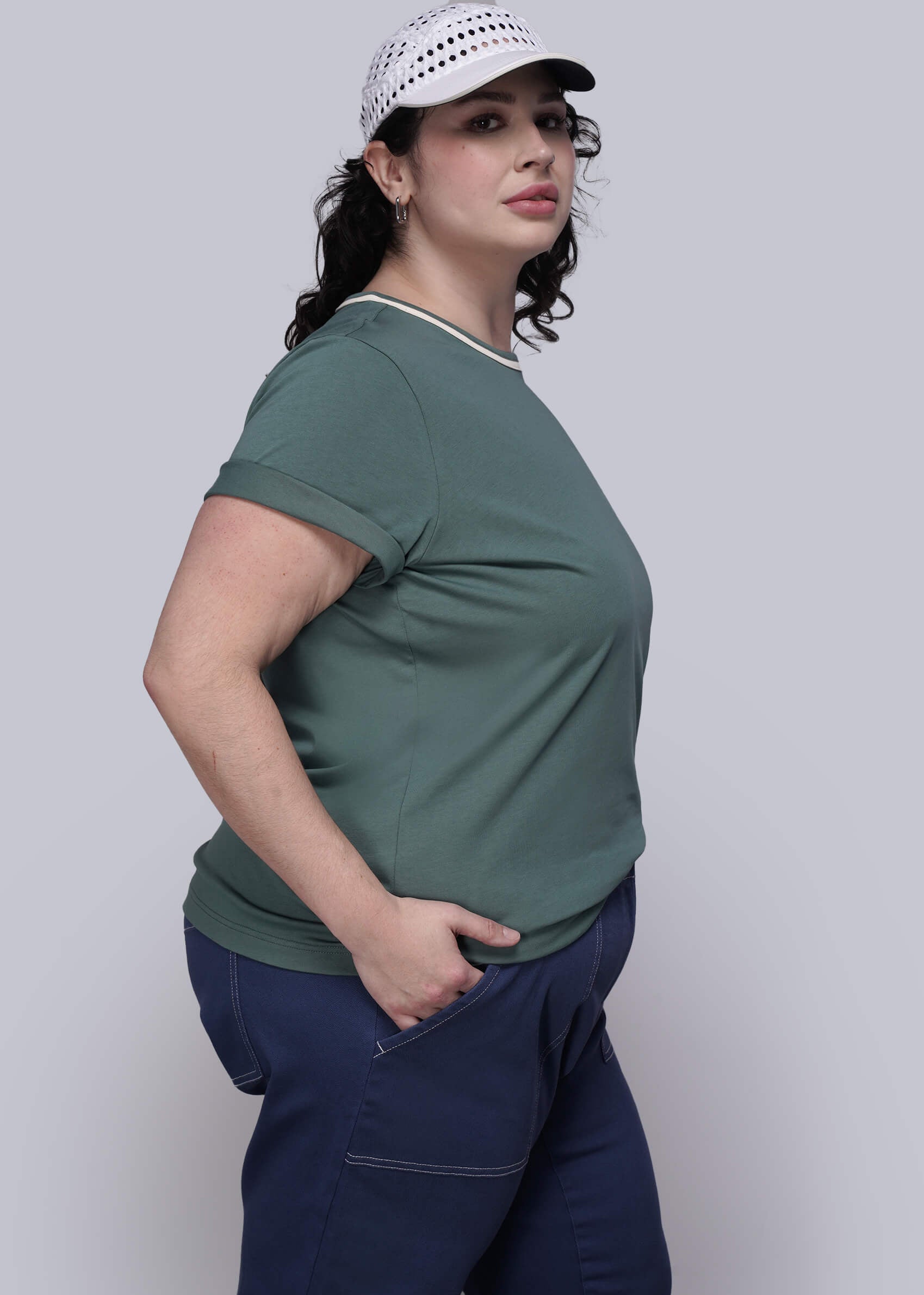 1X=Person wearing a green shirt and navy pants with a white cap on a plain background