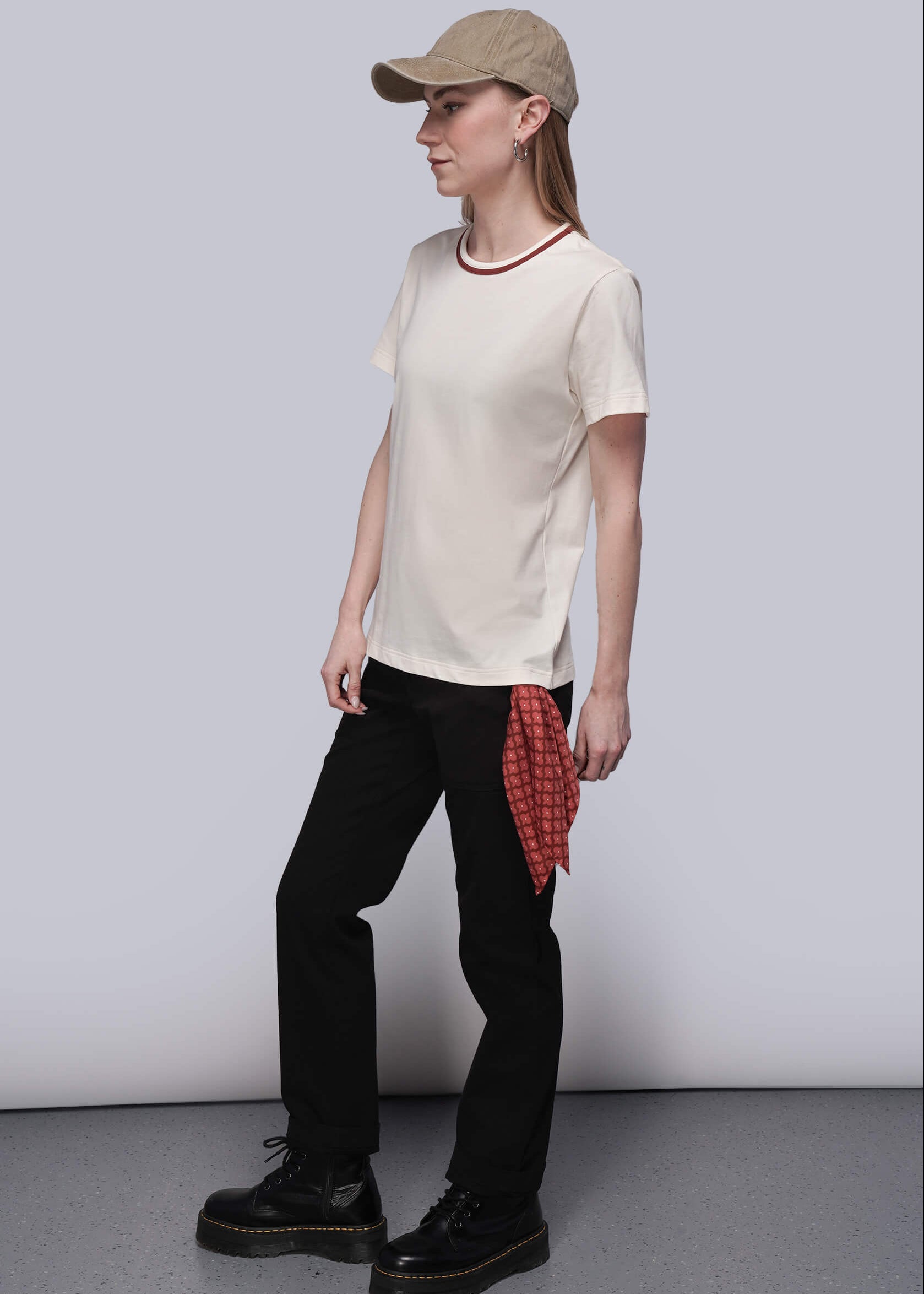 S=Person wearing a beige cap, white t-shirt, black pants, and black shoes on a plain background