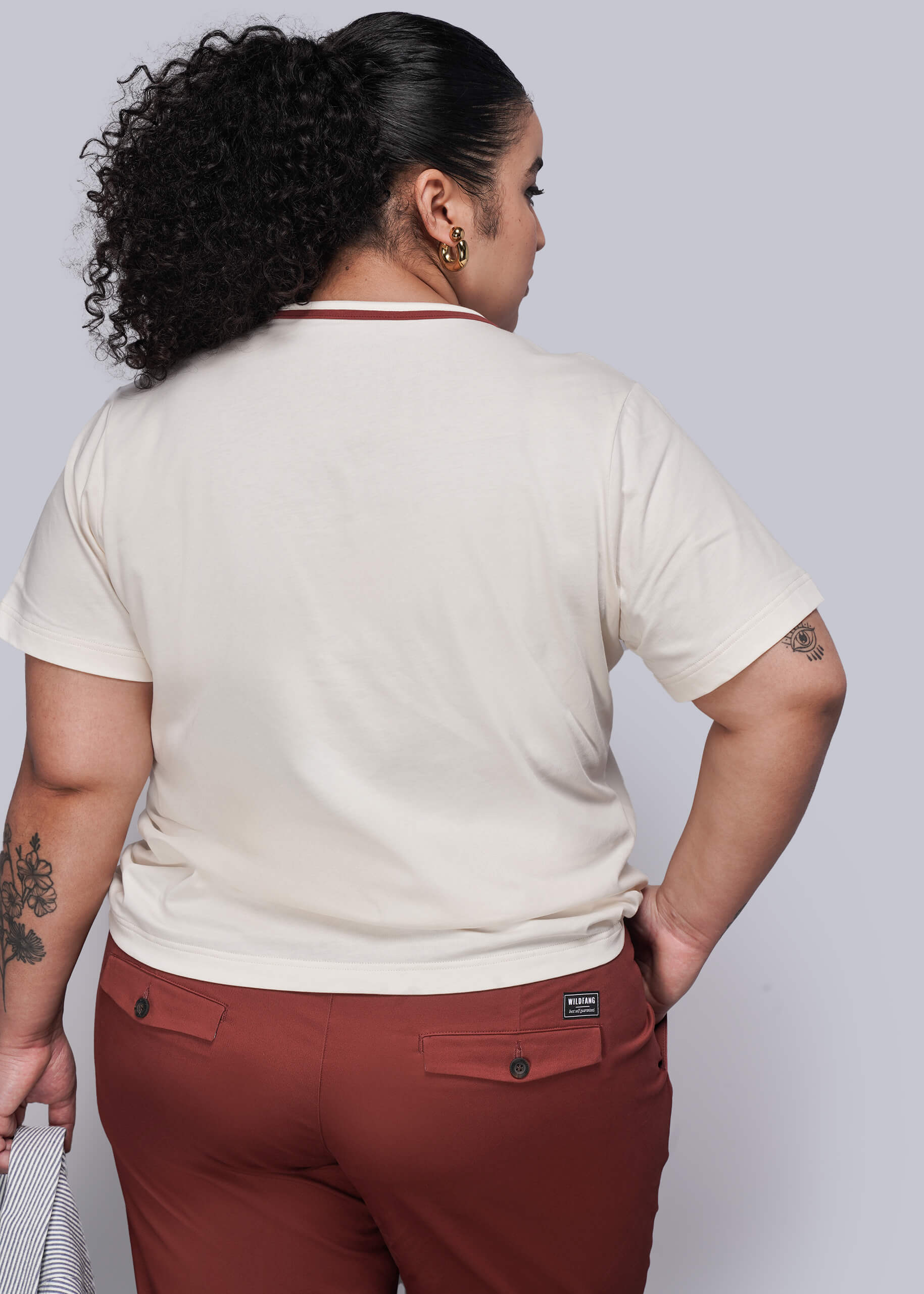 1X=Person wearing a beige t-shirt and red pants against a plain background