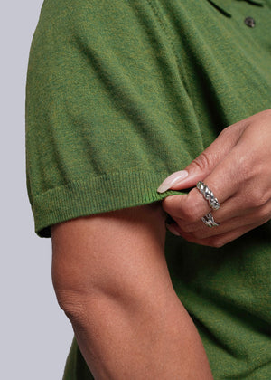 1X=Close-up of a person wearing a green sweater with a neutral background