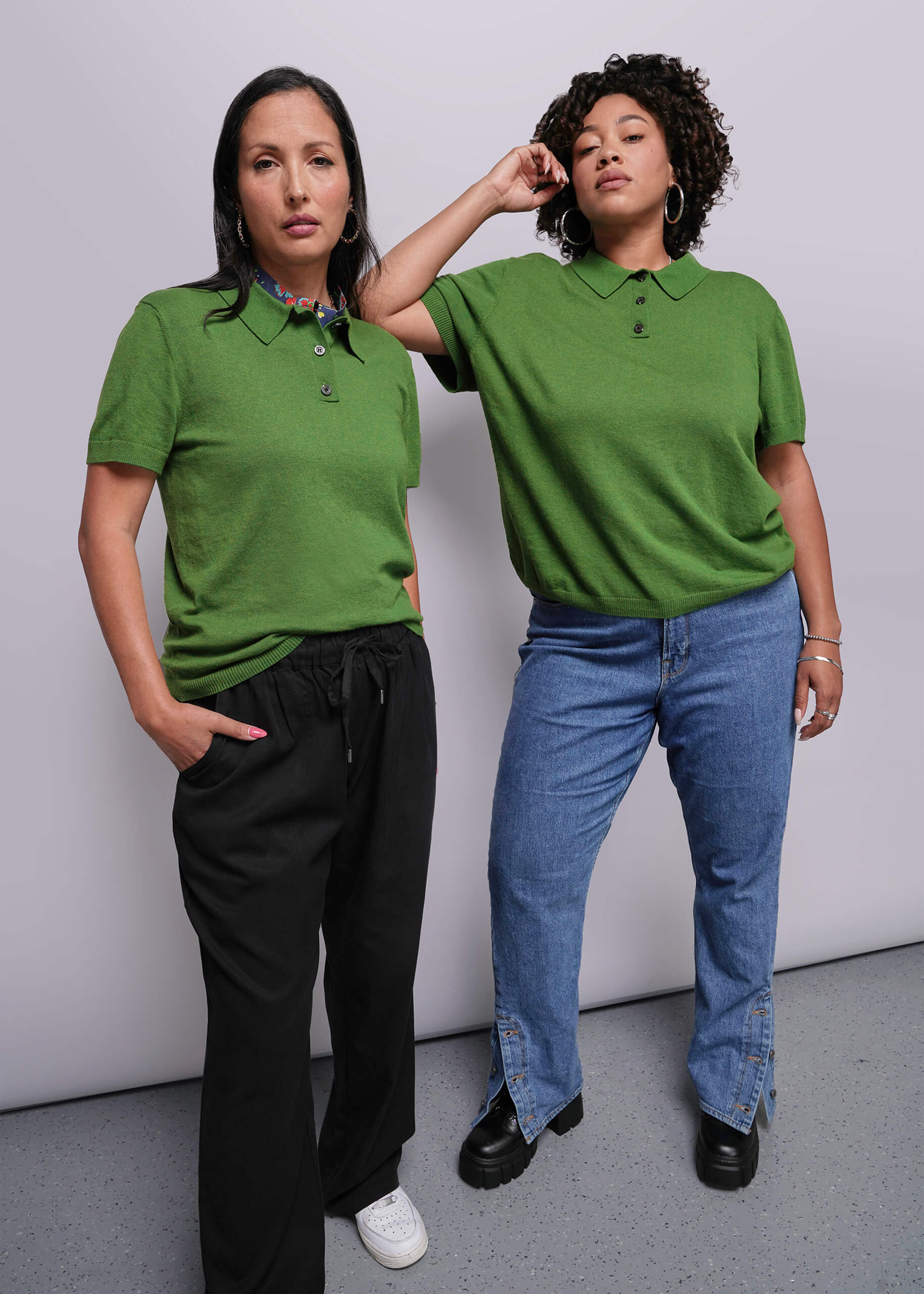 Two people wearing green polo shirts and jeans against a plain background