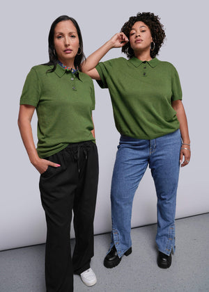 Two people wearing green polo shirts and jeans against a plain background