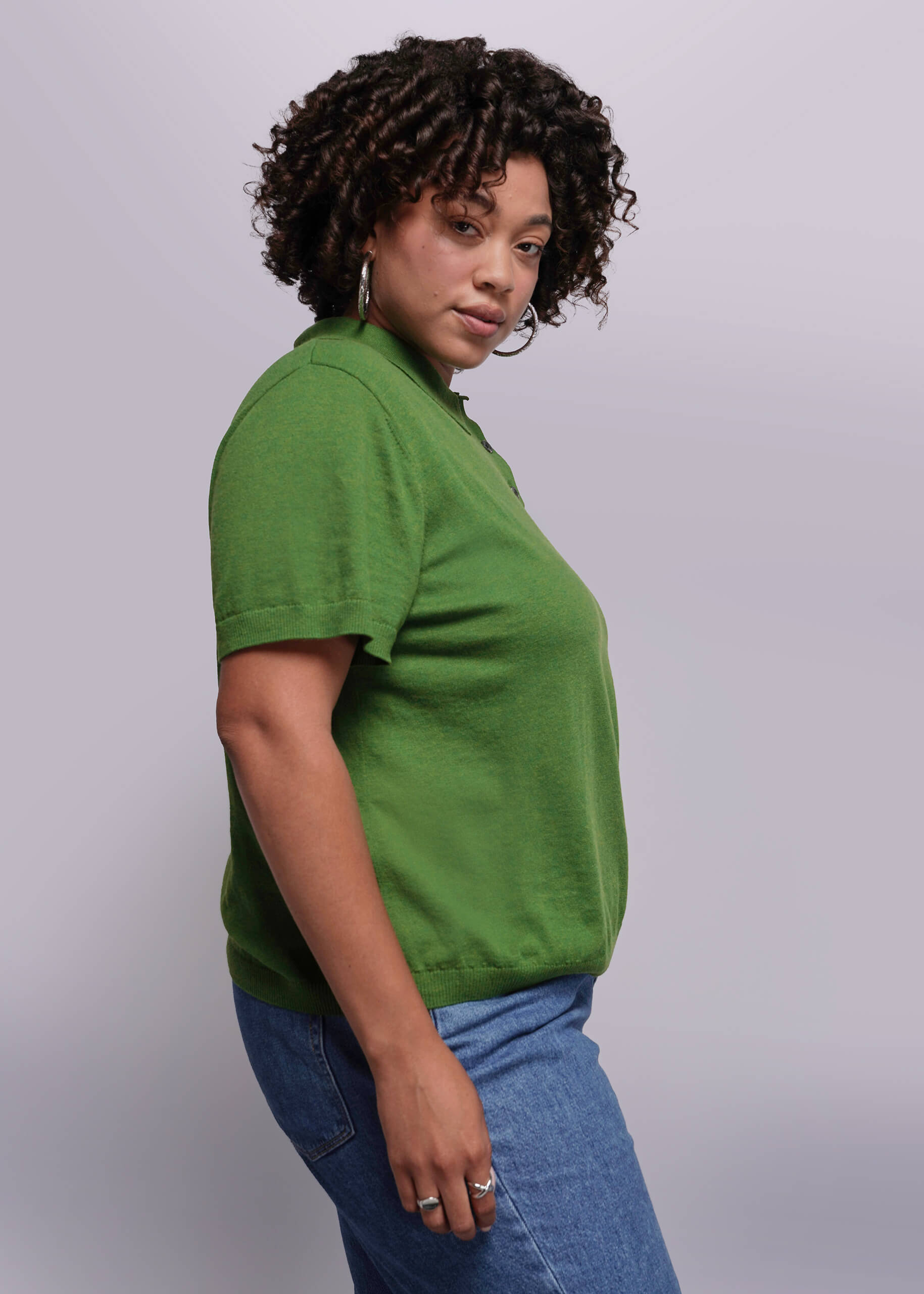 1X=Woman wearing a green polo shirt and blue jeans against a plain background