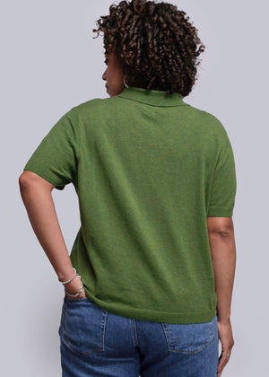 1X=Person wearing a green polo shirt and blue jeans against a plain background