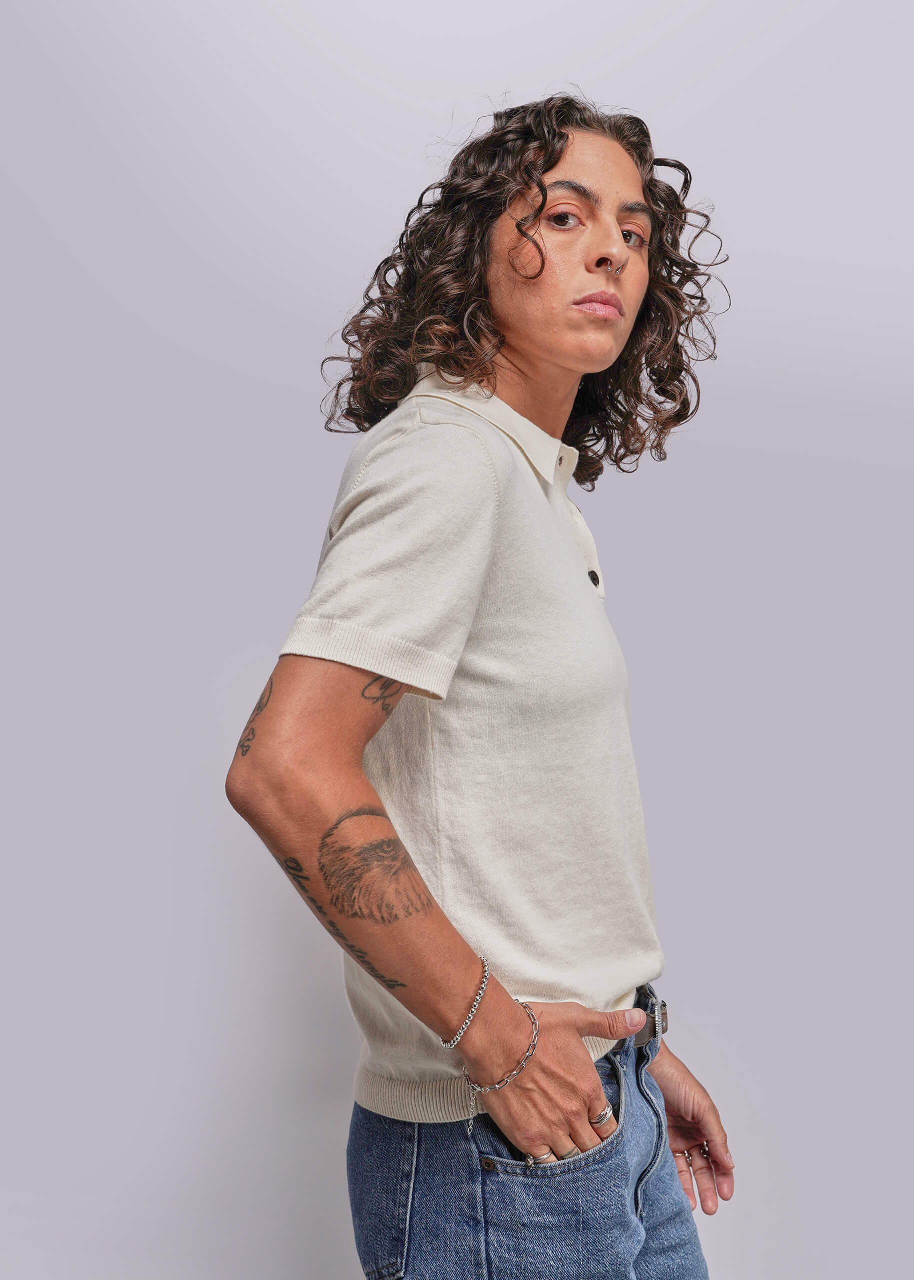 S=Person wearing a light-colored polo shirt and blue jeans against a plain background