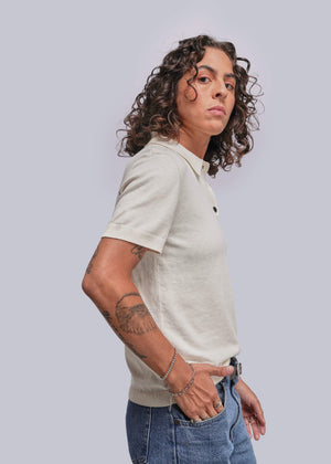 S=Person wearing a light-colored polo shirt and blue jeans against a plain background