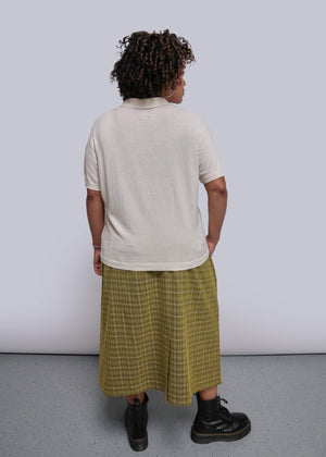 1X=Person wearing a white t-shirt and yellow plaid skirt against a plain background