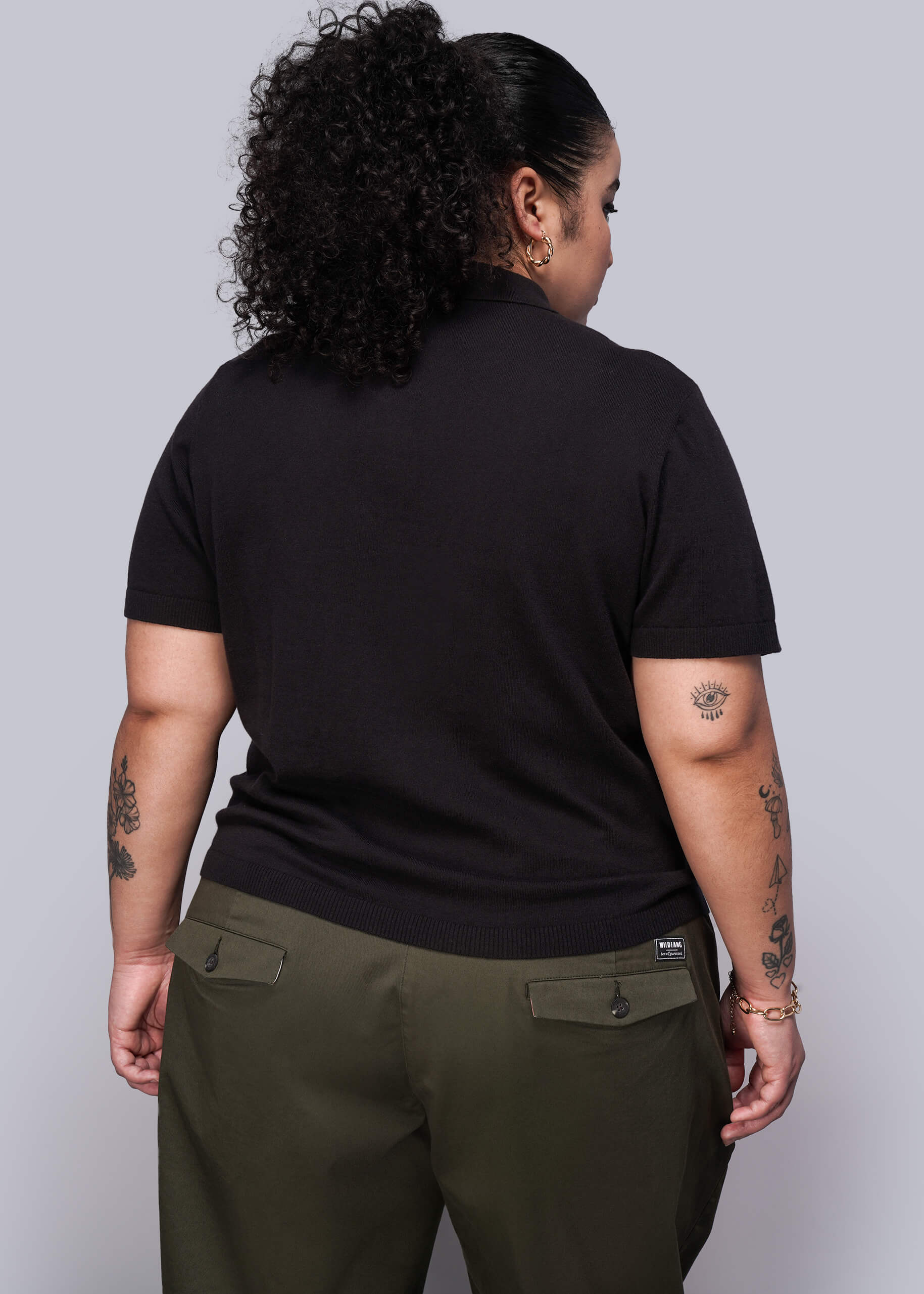 1X=Person wearing a black sweater and green pants against a plain background