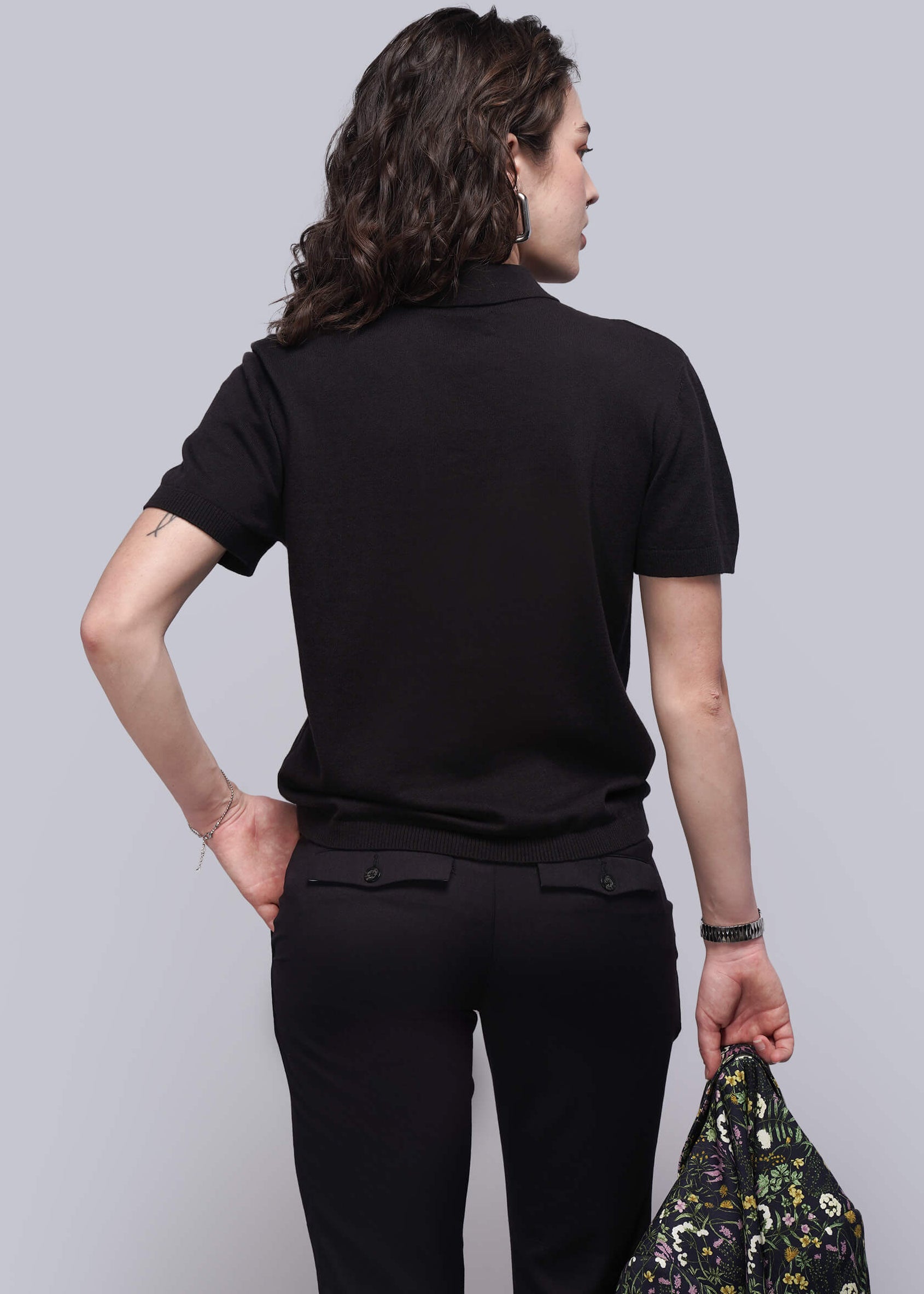 S=Person wearing a black outfit holding a floral-patterned jacket against a plain background