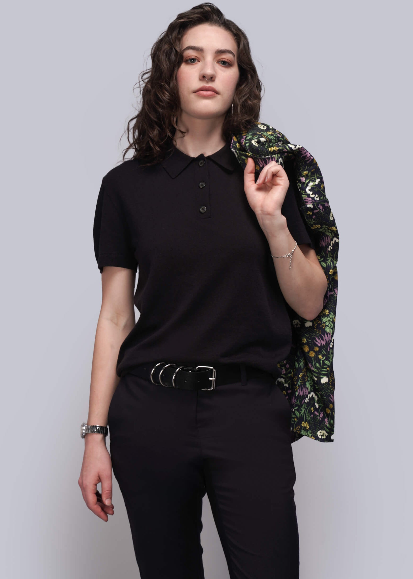 S=Person wearing a black sweater and pants with a floral jacket on a plain background