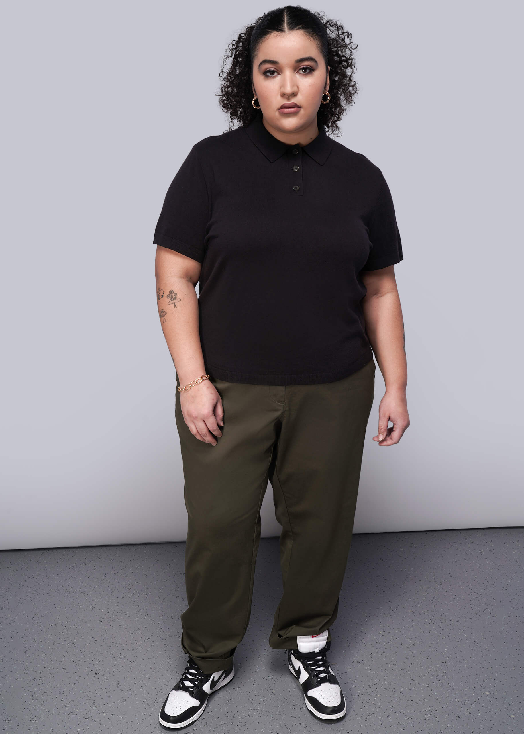 1X=Person wearing a black polo shirt and green pants against a plain background