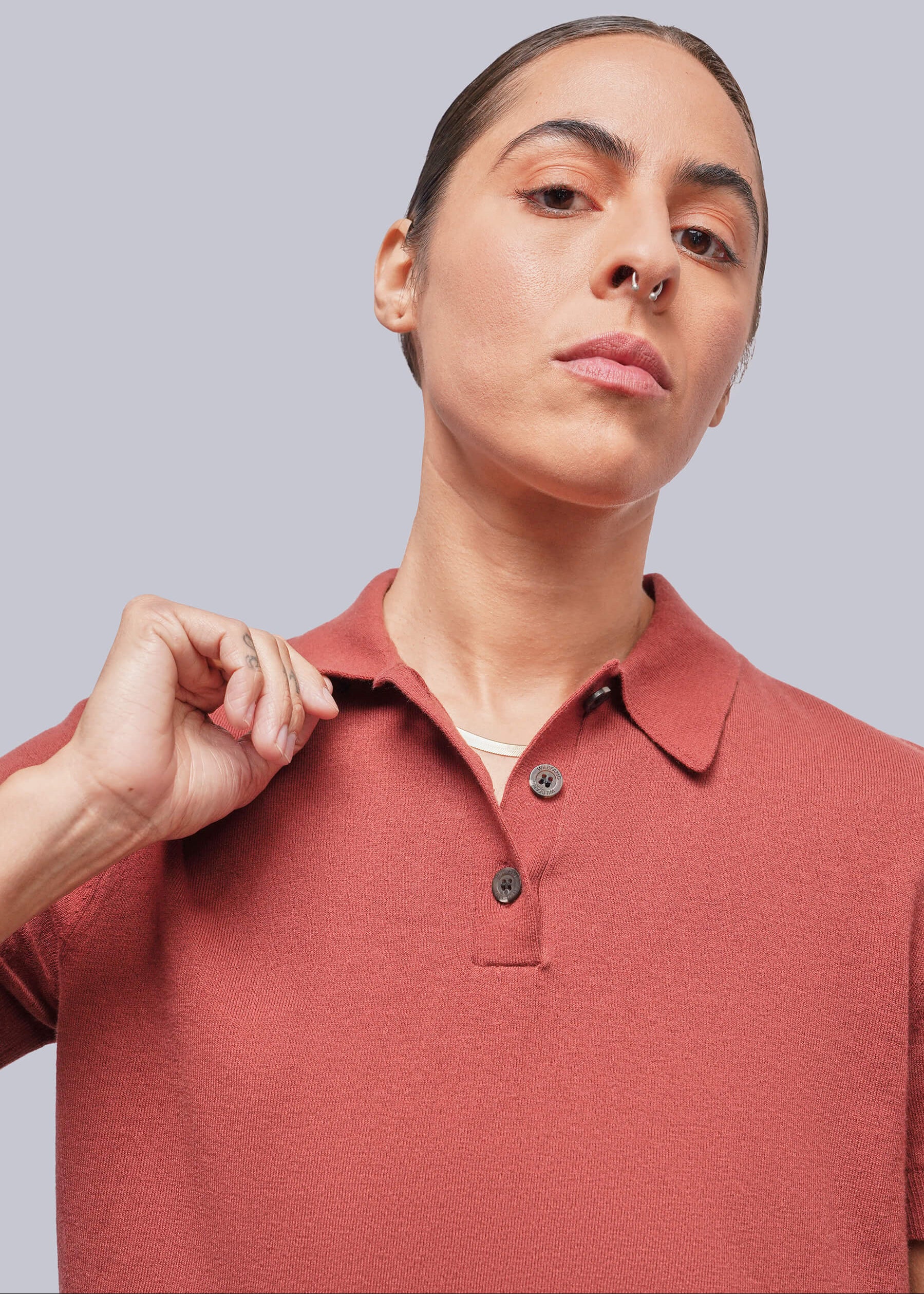 A close-up of a model wearing a short-sleeve polo shirt in a muted terracotta color, set against a solid light gray background.