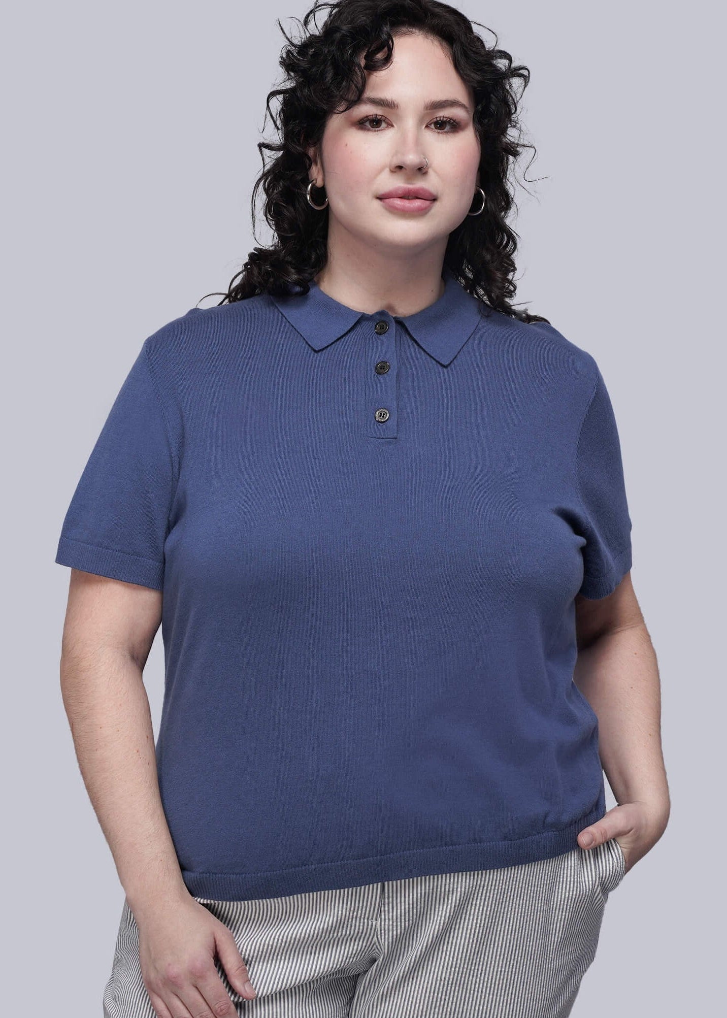 1X=Woman wearing a blue polo shirt and gray checkered pants on a light gray background