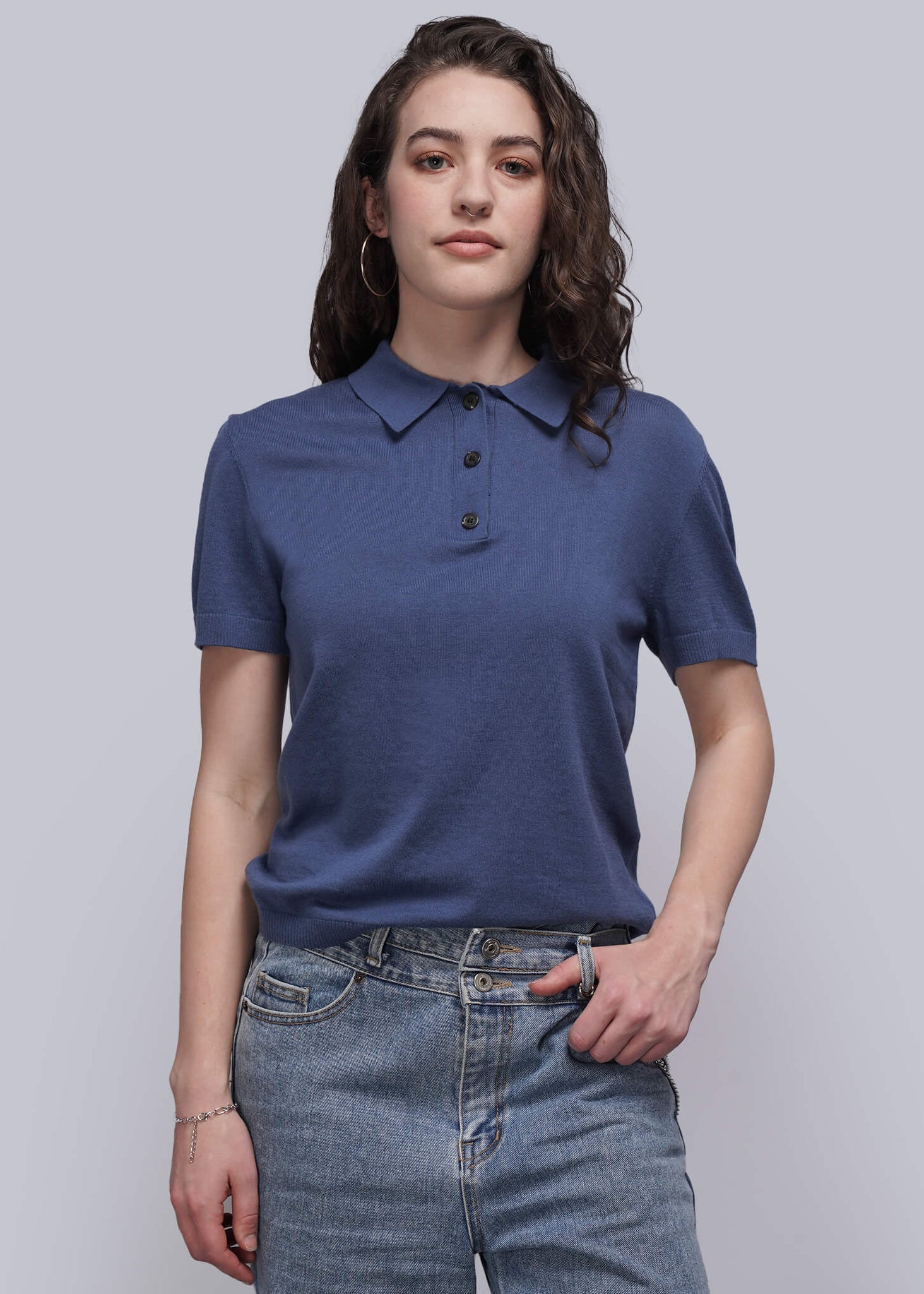 Woman wearing a blue polo shirt and jeans against a plain background