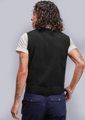 S=Person wearing a black vest over a white shirt with dark blue pants on a plain background
