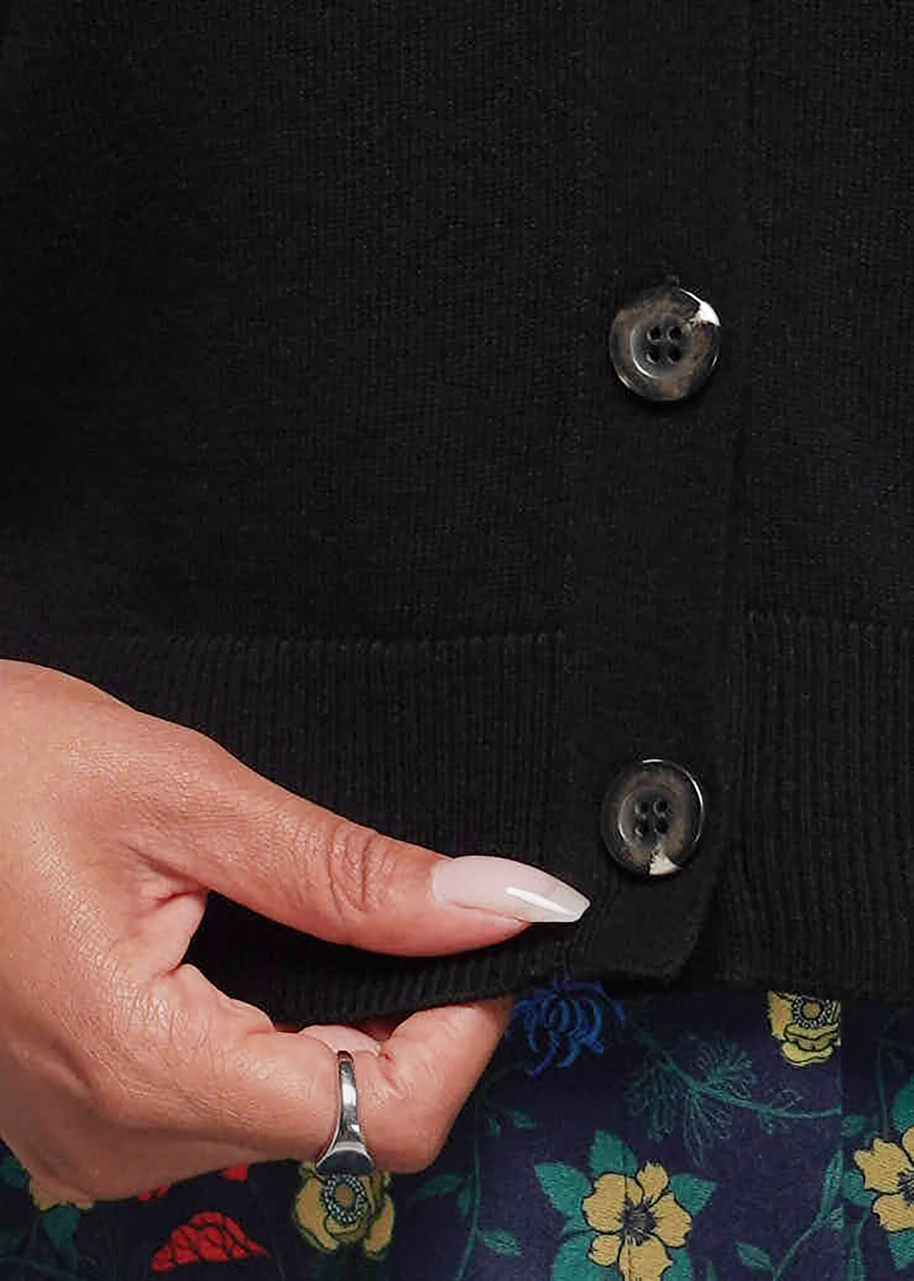 1X=Hand buttoning a black sweater vest with floral-patterned pants underneath