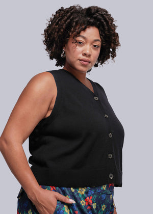 1X=Woman wearing a black sleeveless sweater vest top with buttons against a plain background