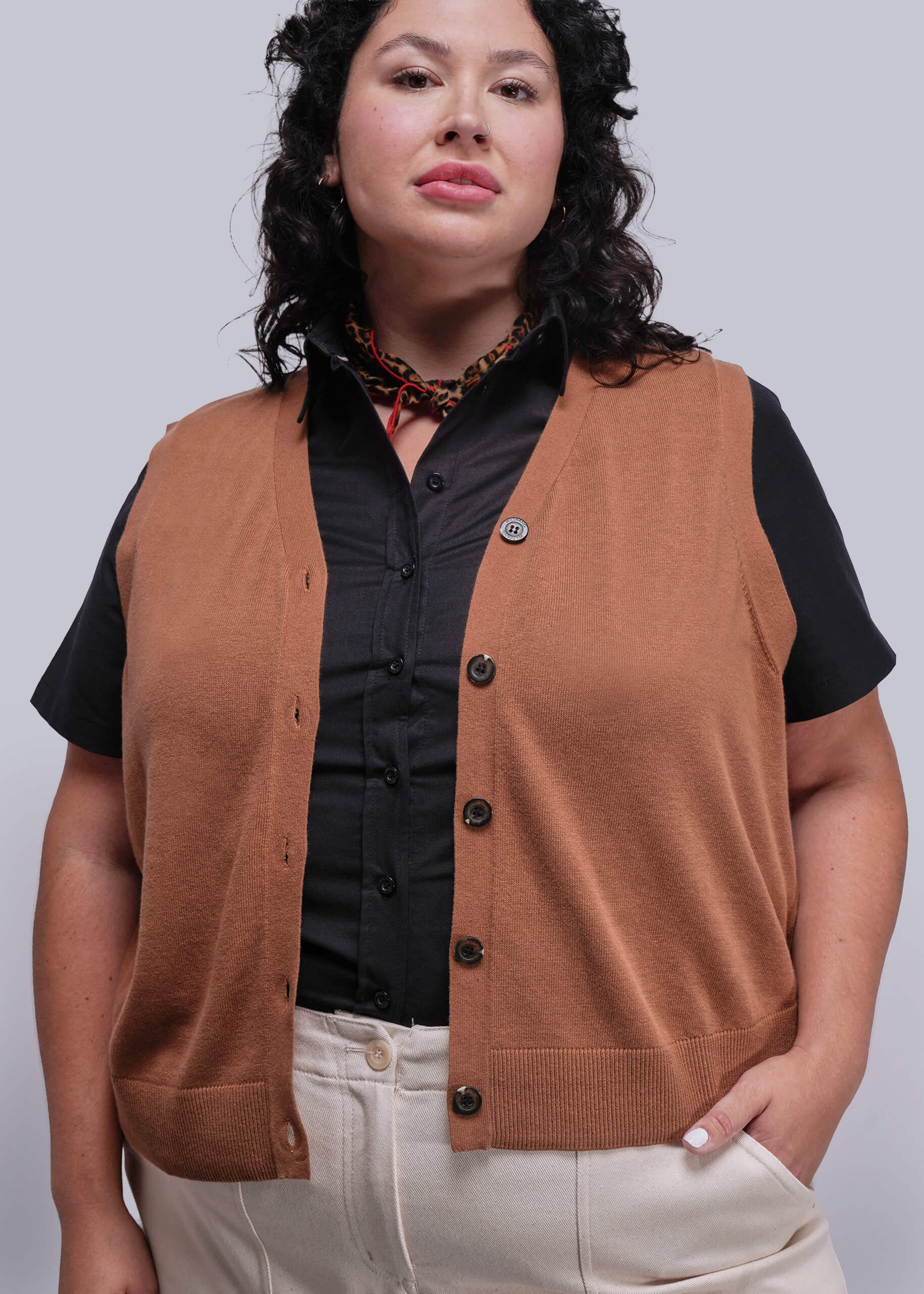 1X=Person wearing a brown vest over a black shirt with a plain background