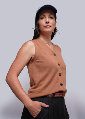 S=Woman wearing a brown sleeveless sweater vest with buttons and a blue cap against a plain background