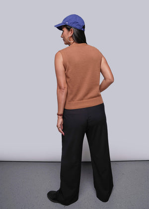 S=Person wearing a brown sleeveless top and black pants with a blue cap, standing against a plain background.