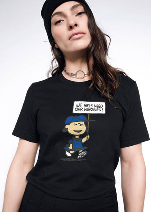 S= Person with long brown hair wears black beanie and The Peanuts x Wildfang Heroines Graphic Tee, which is a black tee that features a graphic of Lucy with a sign that says 