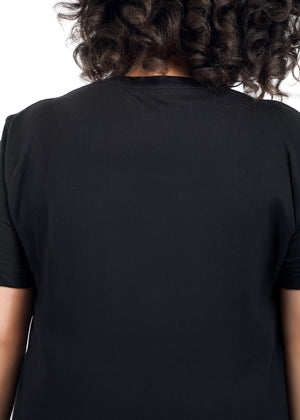 1X=Close up, back view of person with short curly brown hair wearing The Peanuts x Wildfang Heroines Graphic Tee, which is a black tee that features a graphic of Lucy with a sign that says 