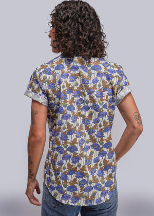 S=Person wearing a floral short-sleeve shirt with blue flowers on a plain background