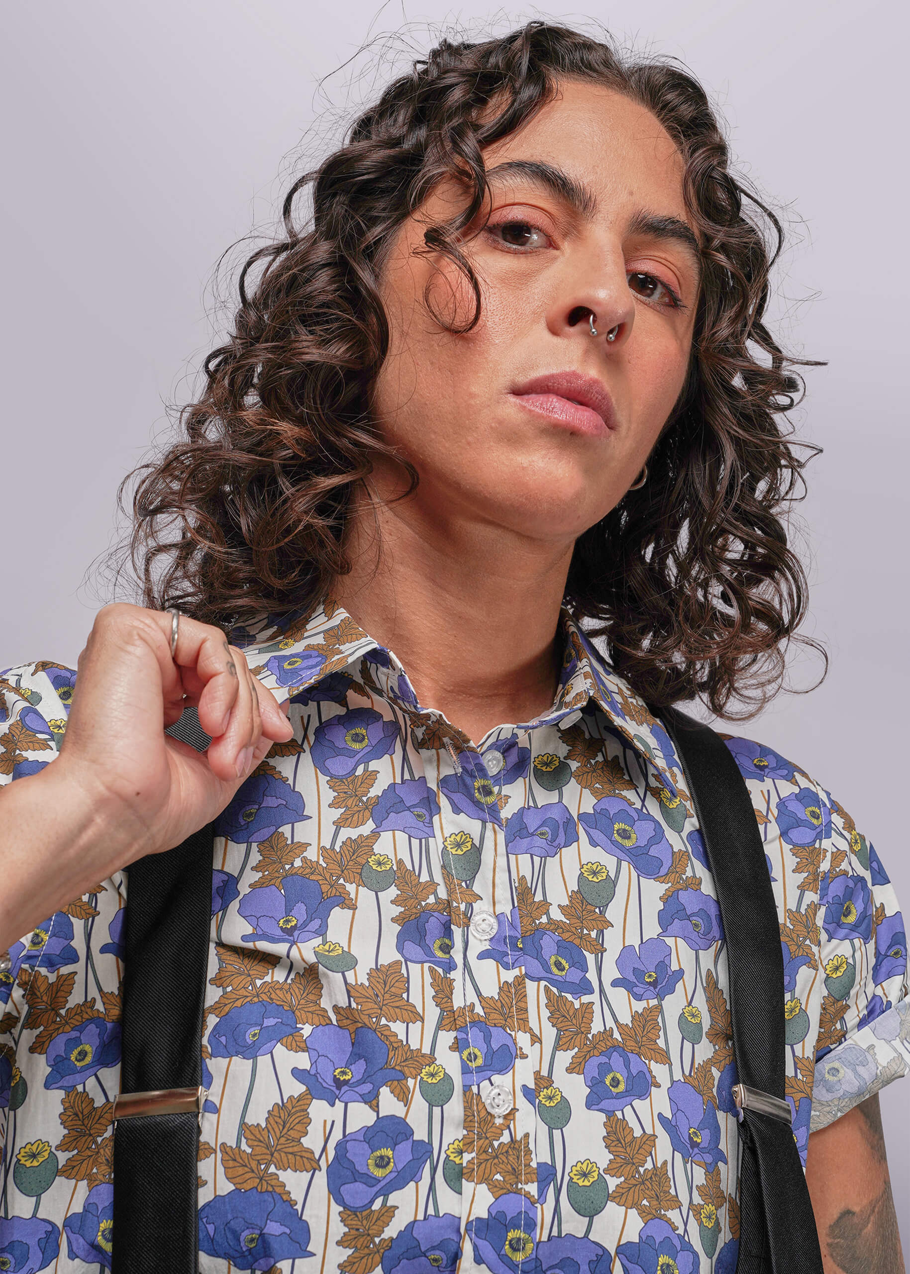 S=Person wearing a floral shirt with blue flowers and suspenders against a plain background