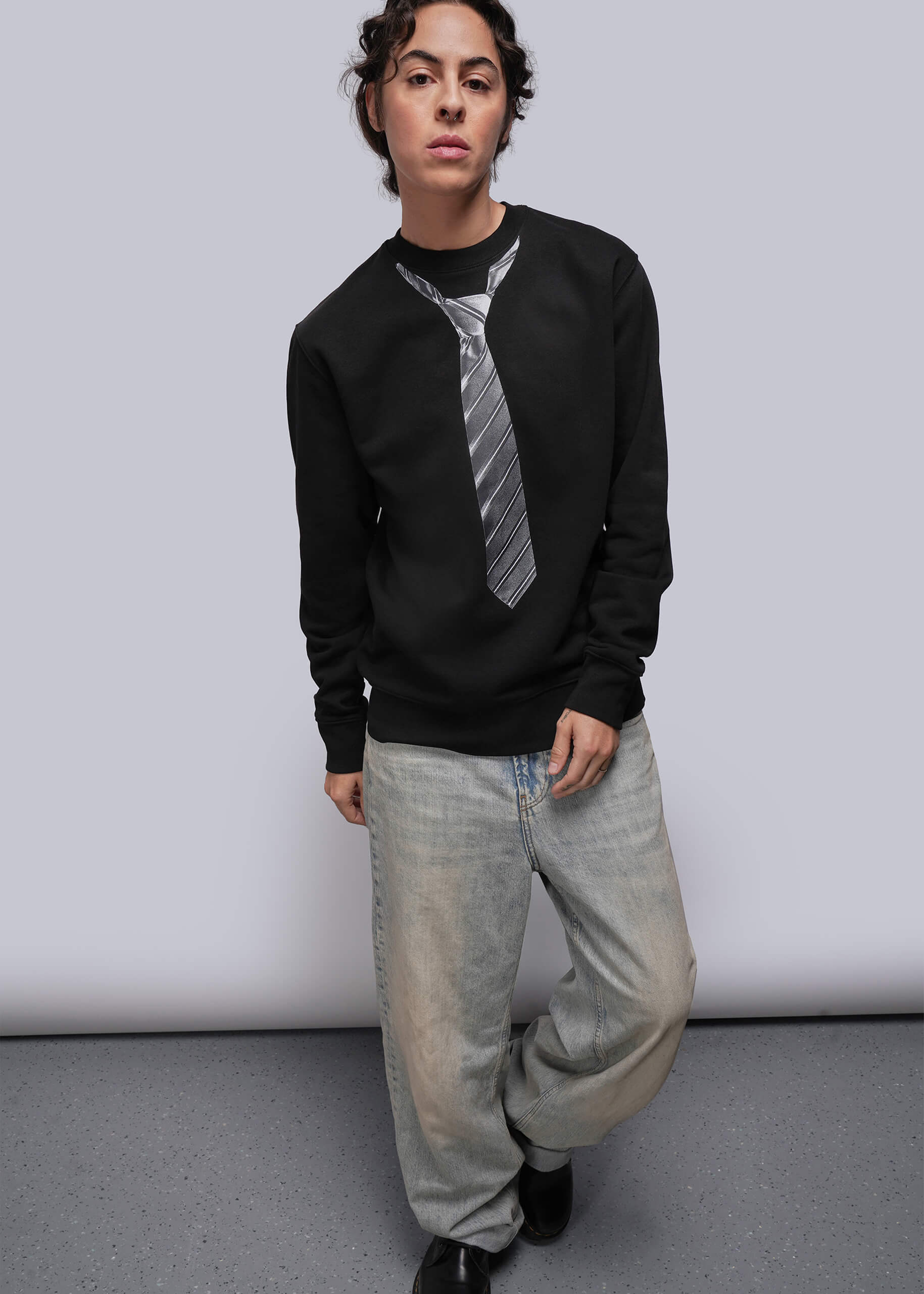 S=Person wearing a black sweatshirt with a tie design and light-colored pants against a plain background