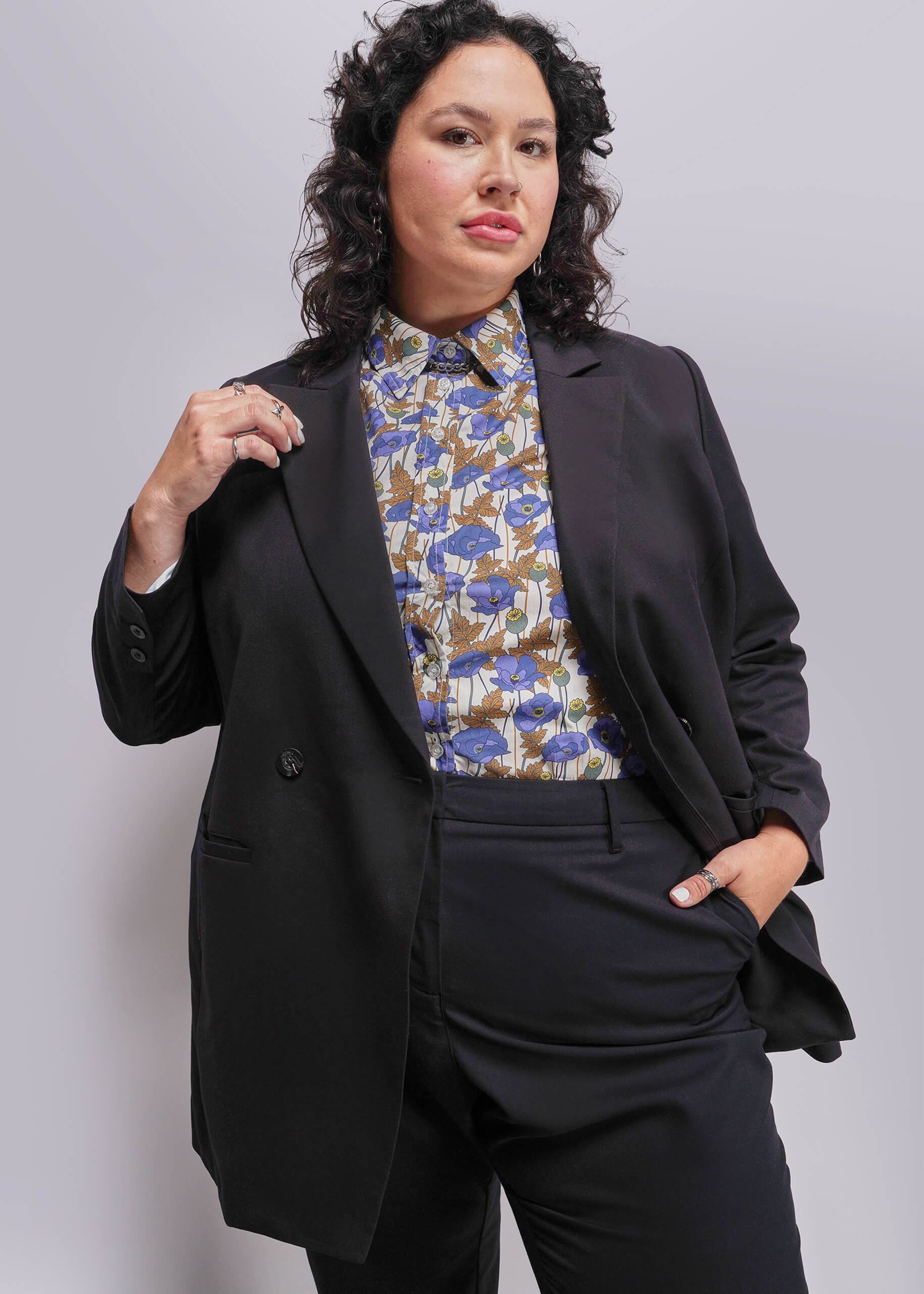 1X=Person wearing a black suit with a floral blouse against a plain background
