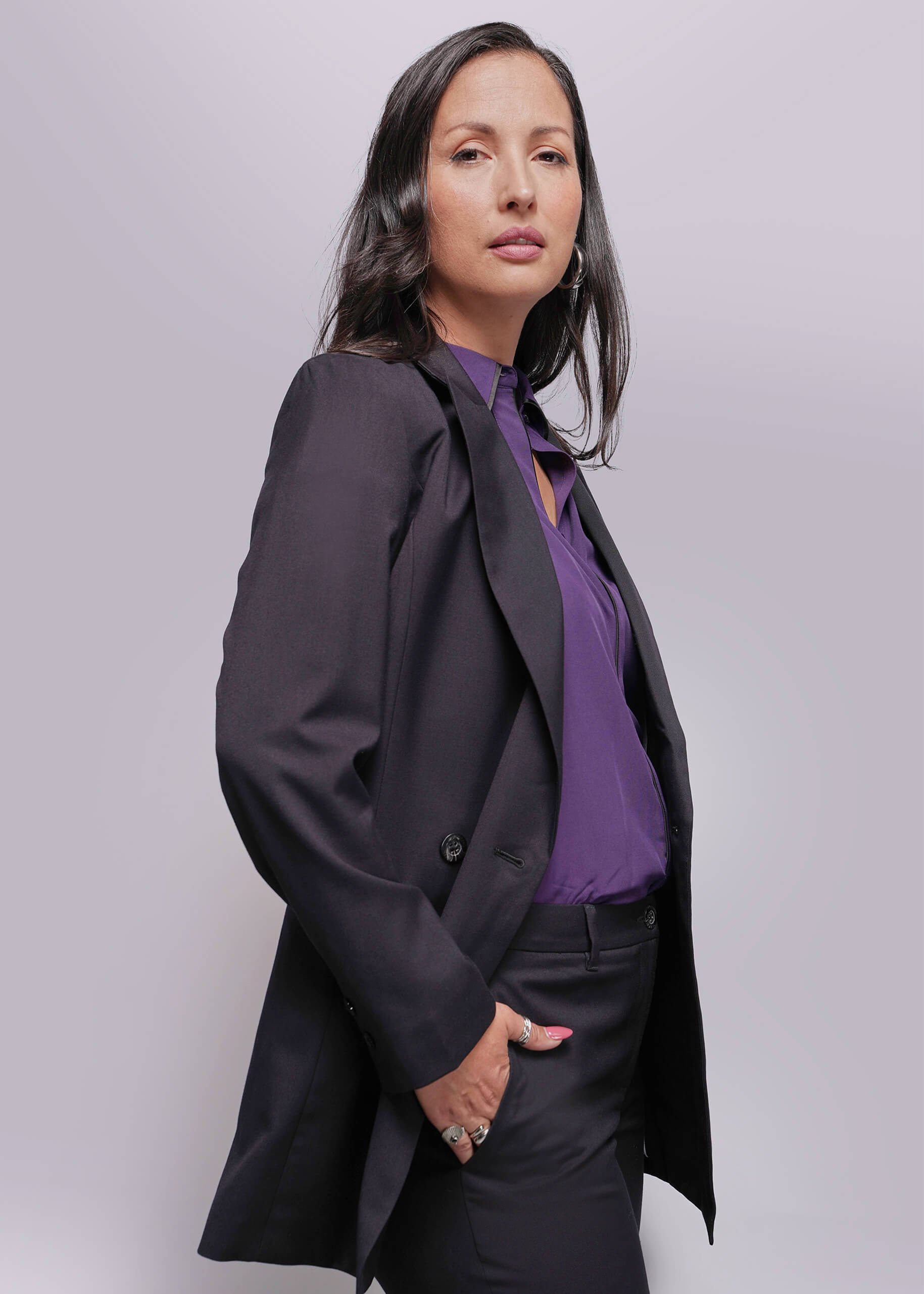 1X=Person wearing a black blazer over a purple shirt against a light gray background