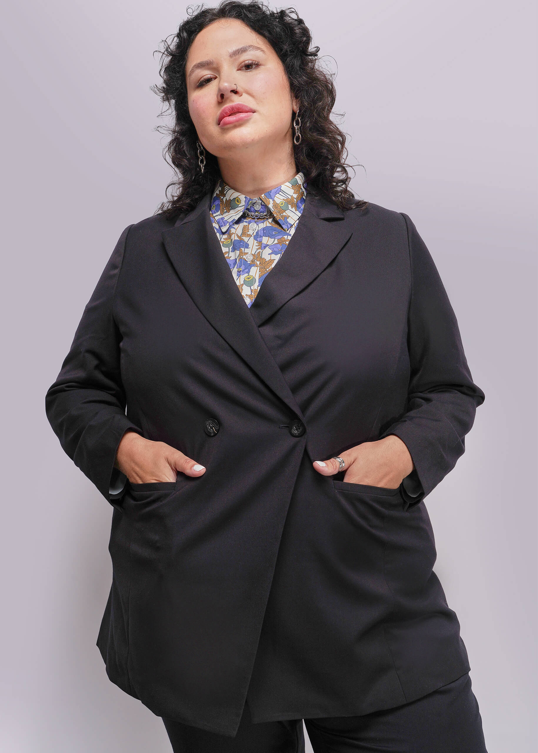 1X=Person wearing a black blazer over a patterned shirt on a plain background