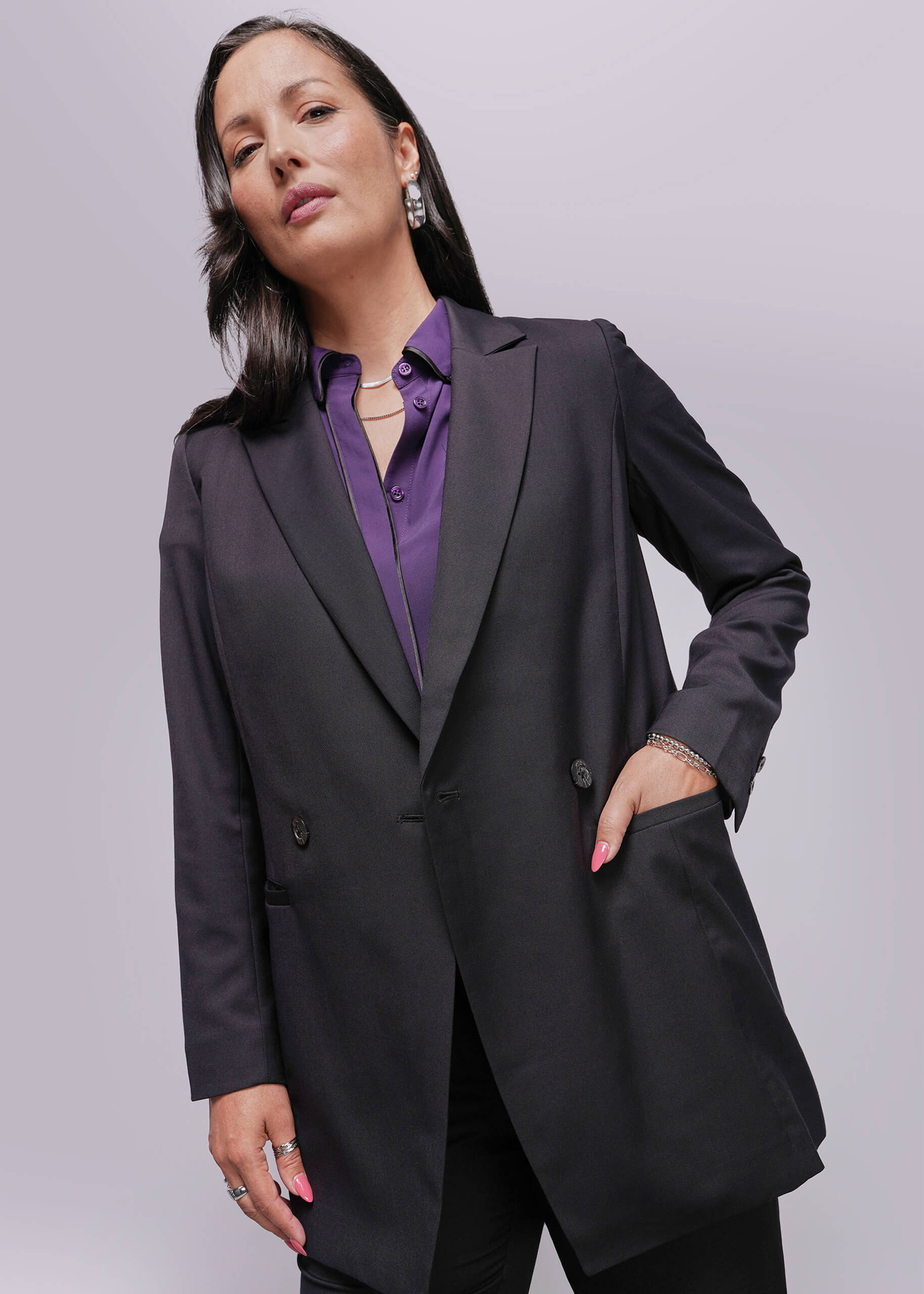 S=Woman wearing a black blazer over a purple shirt against a gray background