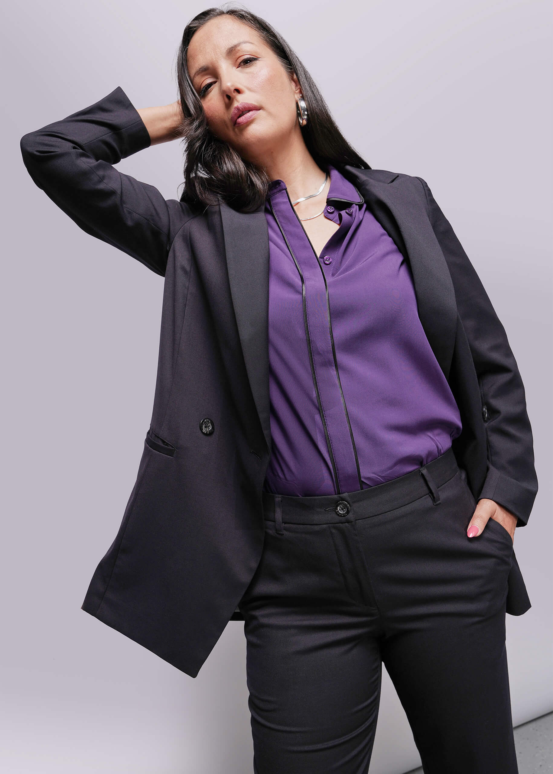 S=Woman wearing a black blazer and purple shirt against a gray background