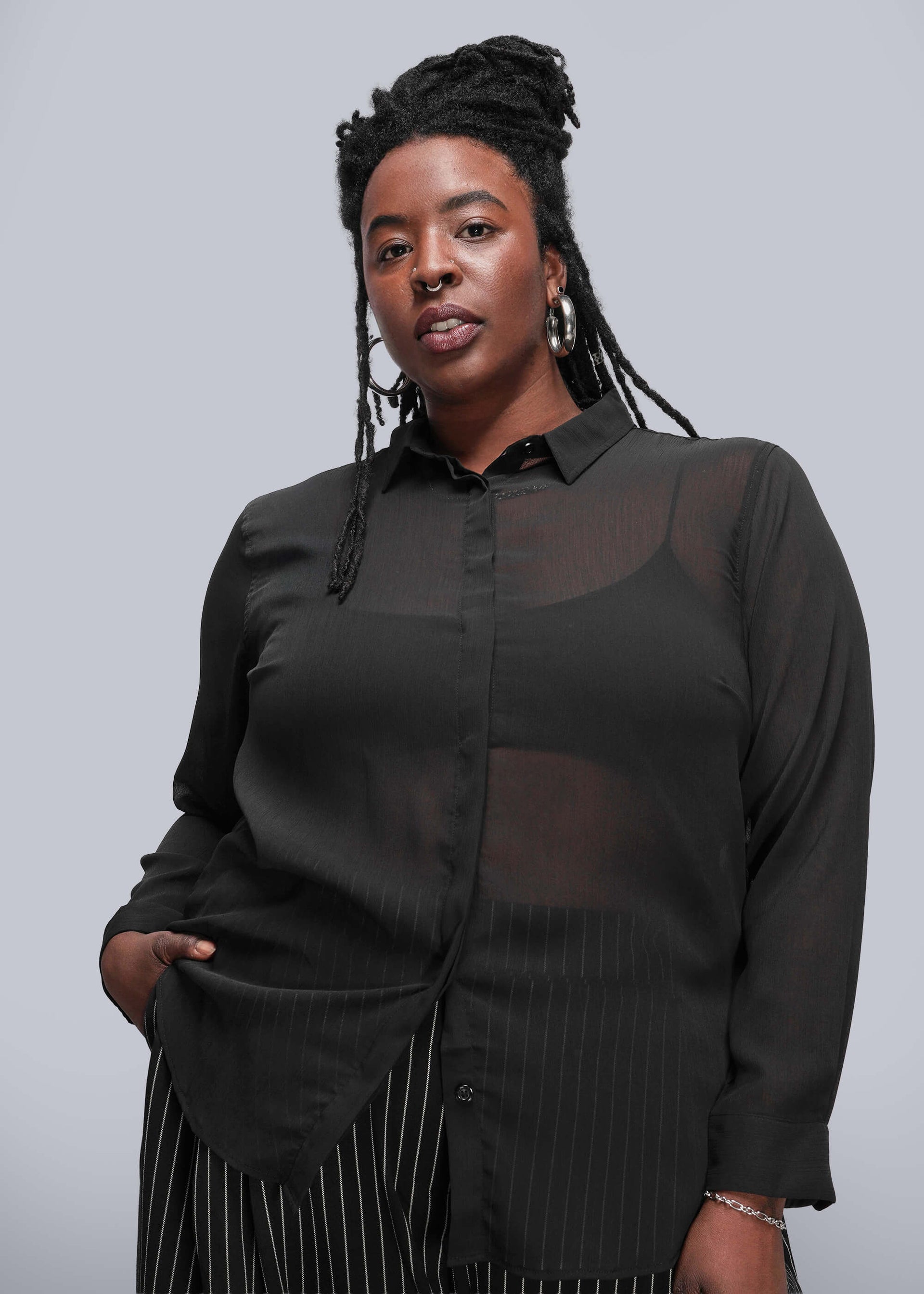 1X=Person wearing a black sheer blouse with long sleeves against a gray background