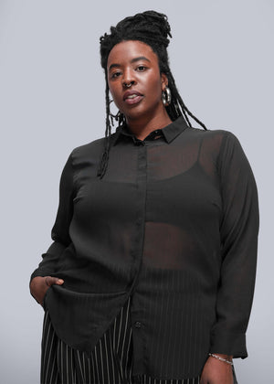 1X=Person wearing a black sheer blouse with long sleeves against a gray background