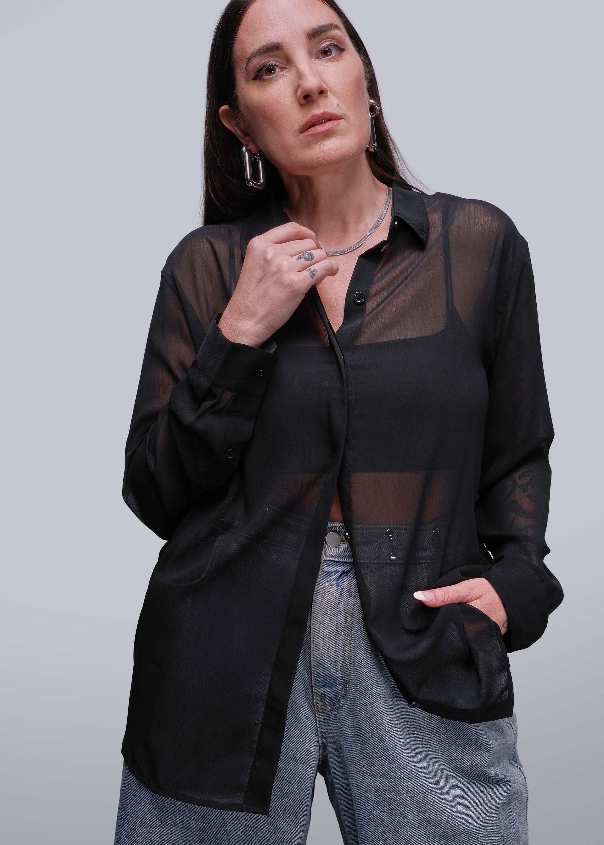S=Person wearing a black sheer blouse over a black shirt with gray pants on a light gray background