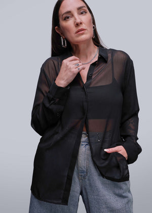 S=Person wearing a black sheer blouse over a black shirt with gray pants on a light gray background