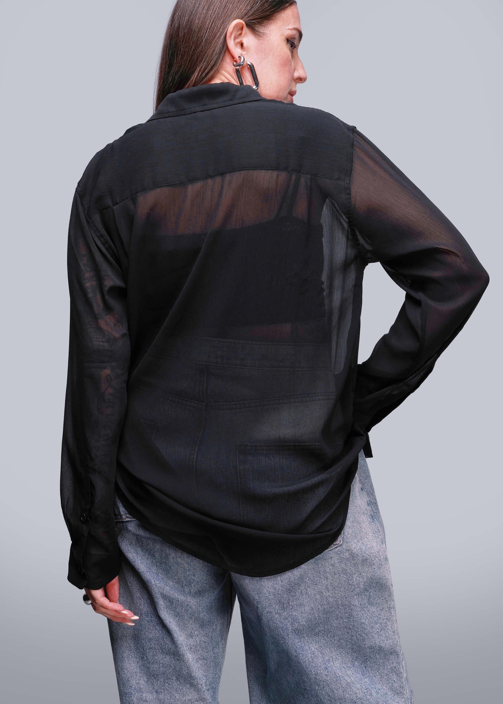 S=Person wearing a black sheer blouse with gray pants on a light gray background