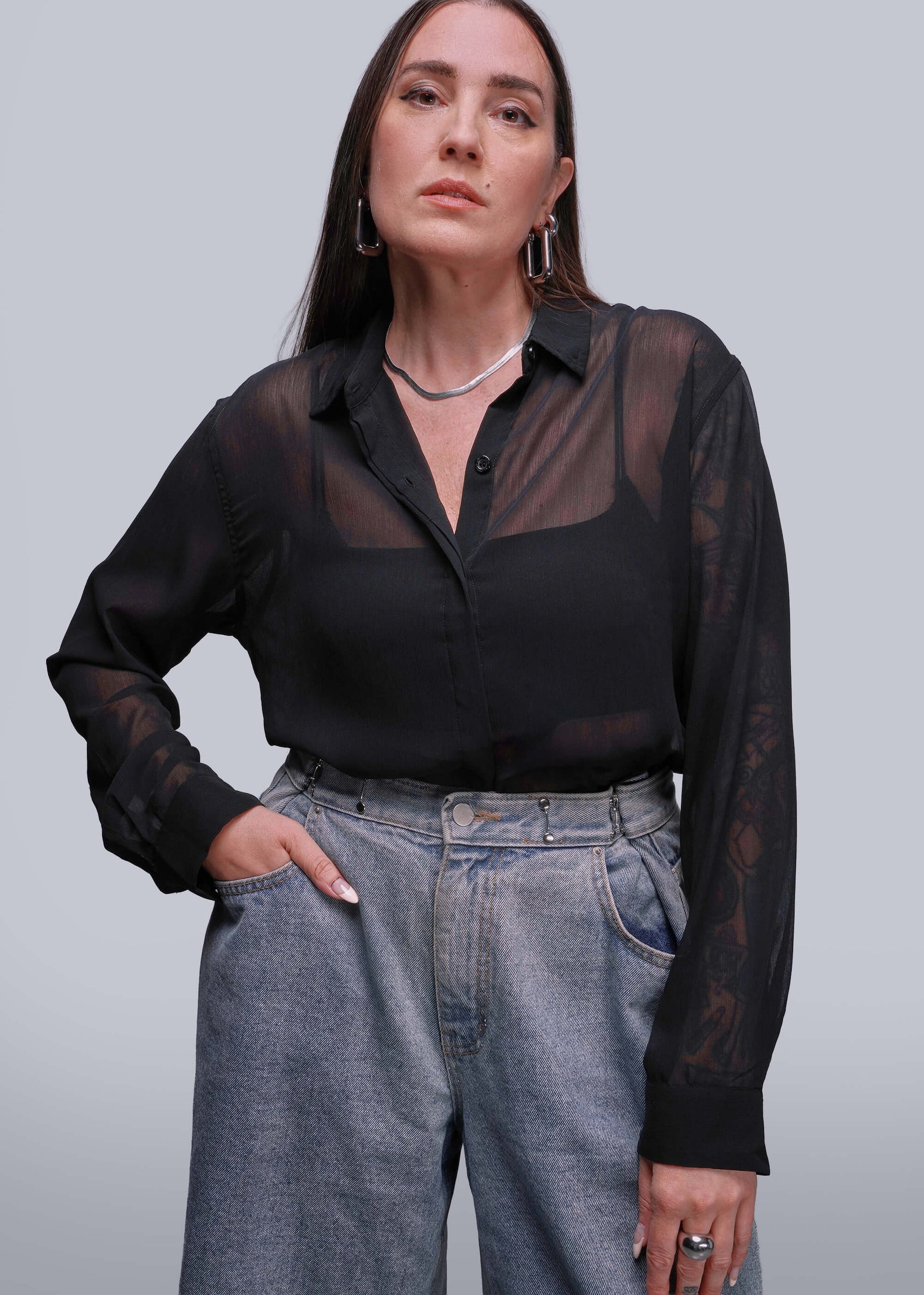 S=Person wearing a black sheer blouse and gray jeans against a plain background