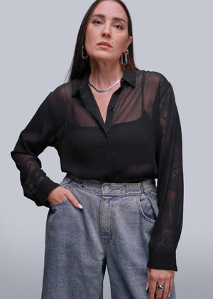 S=Person wearing a black sheer blouse and gray jeans against a plain background