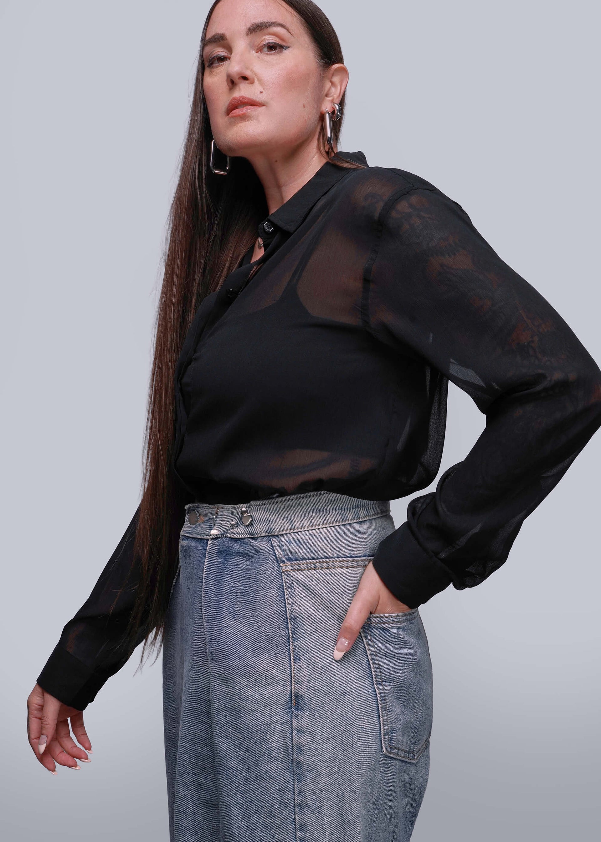S=Person wearing a black sheer blouse and denim skirt against a gray background