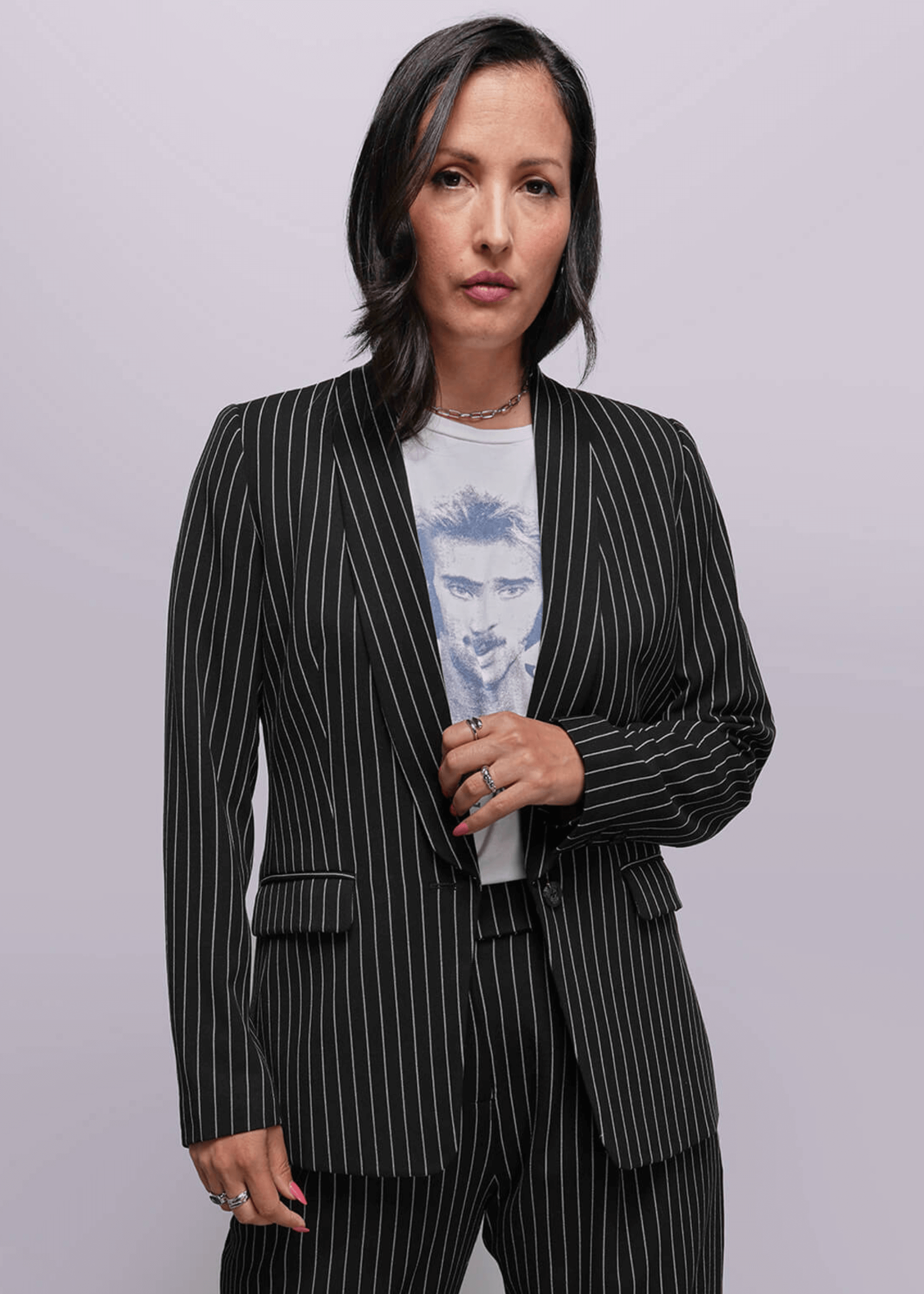 S=Woman wearing a black pinstripe suit over a light blue graphic t-shirt on a gray background
