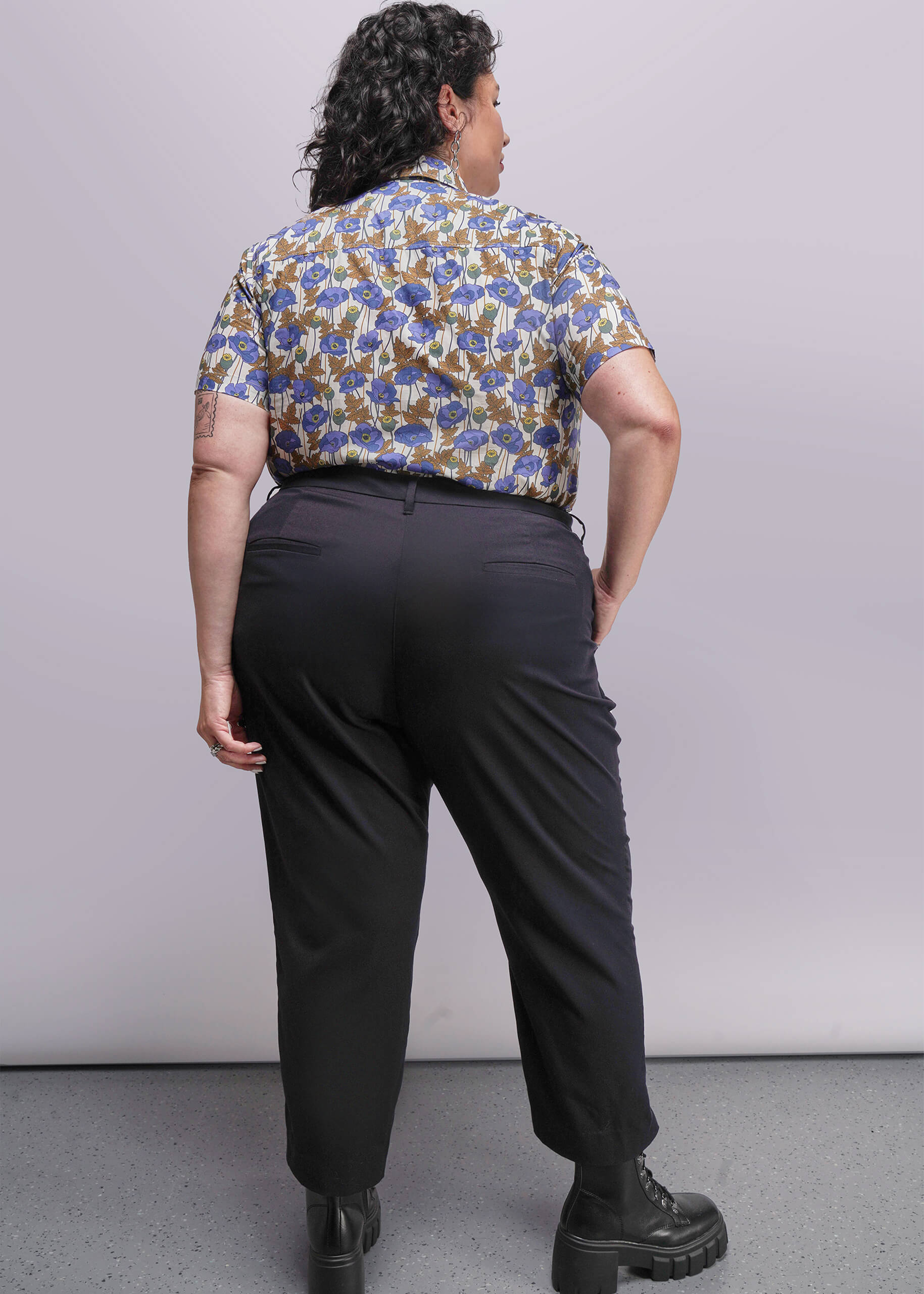 1X=Person wearing a patterned shirt and black pants against a plain background
