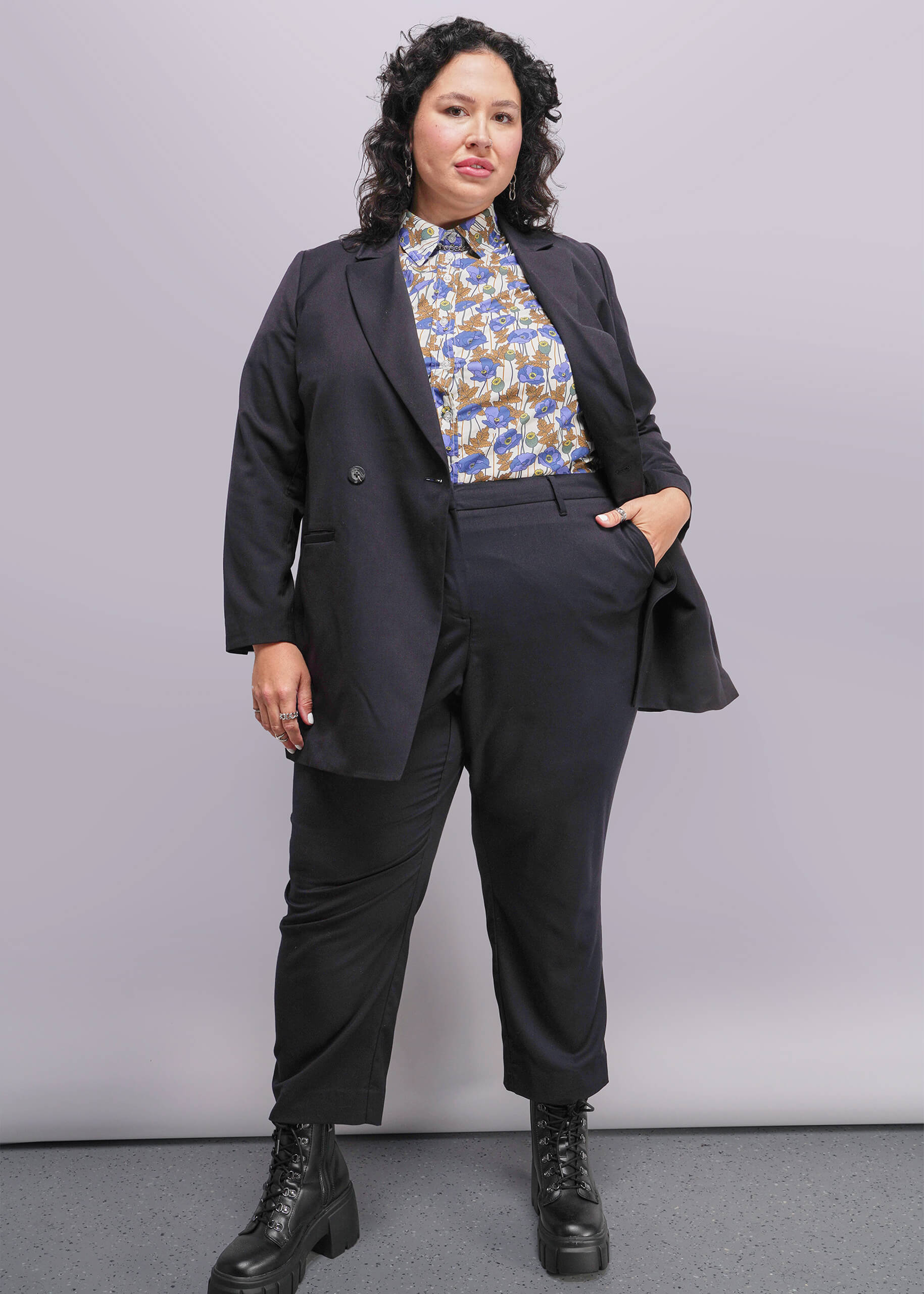 1X=Person wearing a black suit with a patterned blouse against a plain background